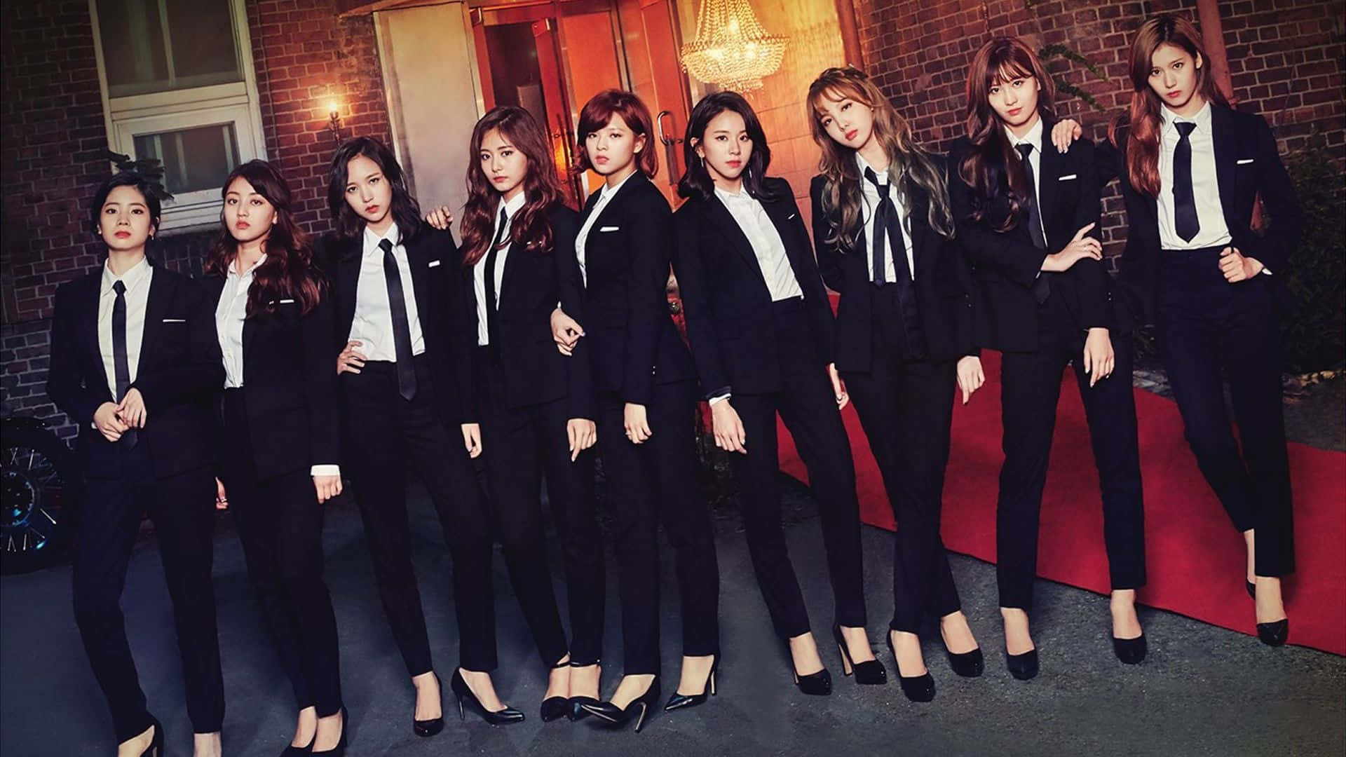2020 Twicelights巡迴演唱會TWICE團體照 壁紙 — 七位身穿利落黑色西裝和白色襯衫的女性在紅地毯上自信地擺姿勢，背景是磚牆。