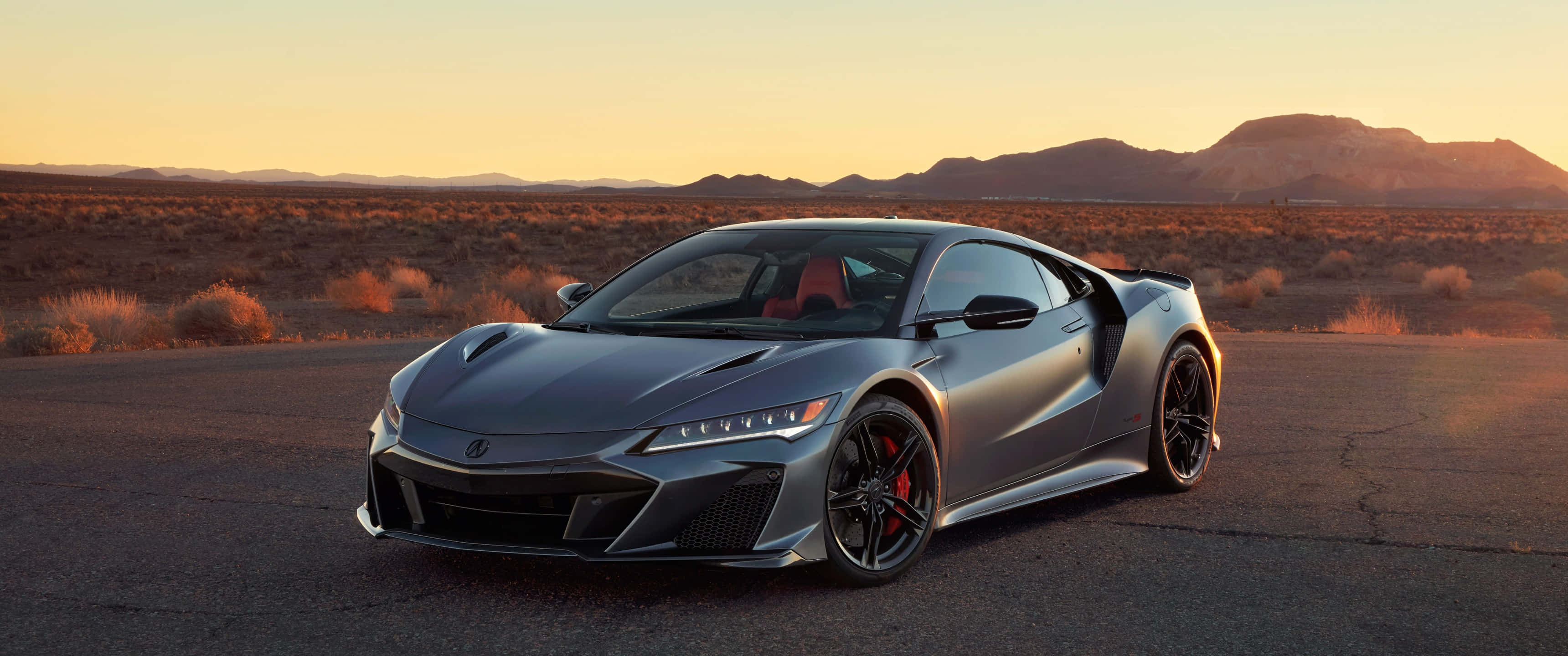 2020款Acura NSX駛過道路 壁紙 — 一輛時尚的銀色跑車帶有紅色點綴，停在沙漠公路上，正值黃金時刻，背景有山脈。
