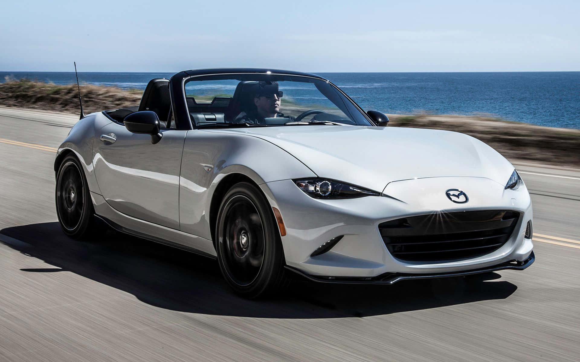 2020年馬自達MX-5 Miata白色跑車 壁紙 — 一輛銀色Mazda MX-5 Miata開篷跑車沿海岸公路飛馳，背景是海洋。