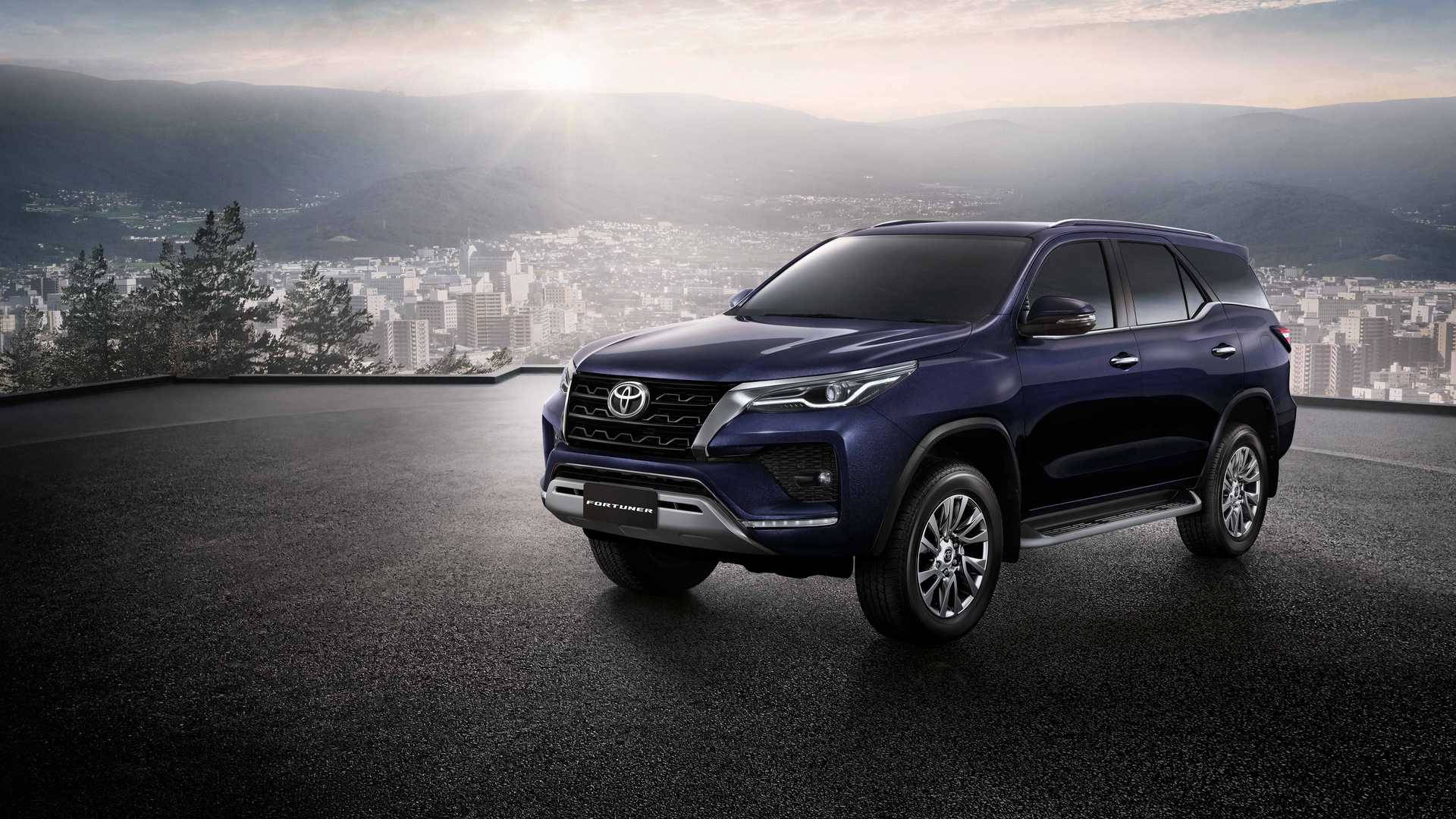 藍色豐田 Fortuner SUV 停泊在屋頂，俯瞰日出時的城市與山巒。