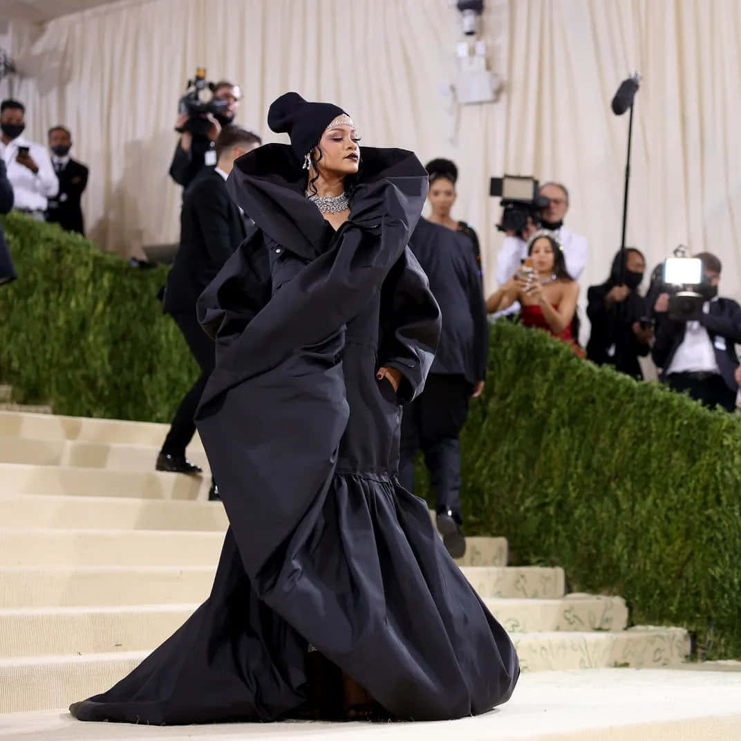 Rihanna 身穿黑色長袍，在正式活動中走下樓梯。