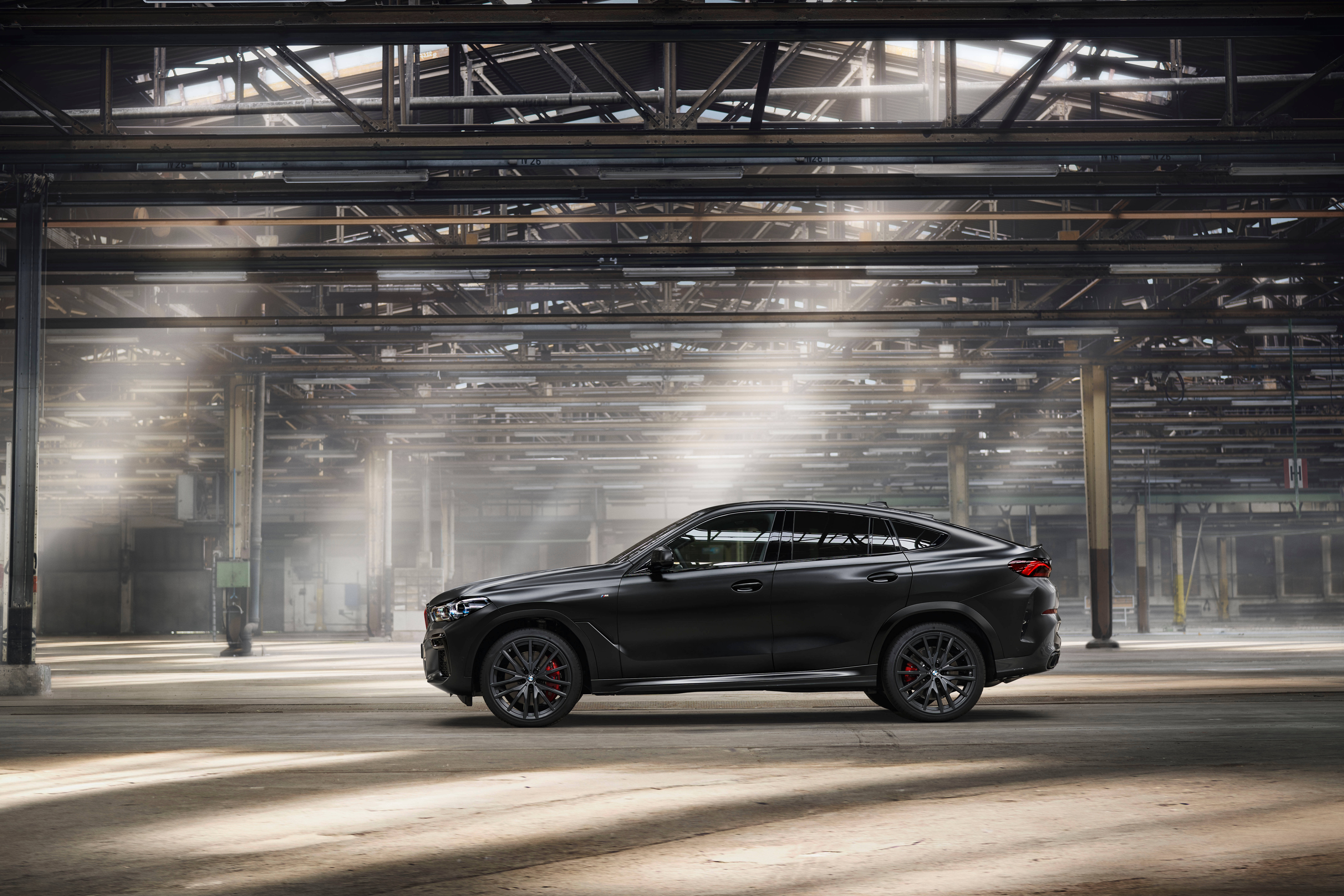 2021 黑色 BMW X6 壁紙 — 一架型格黑色BMW X6 M停泊在陽光普照的廢棄工業倉庫中，有橫樑和塵埃。