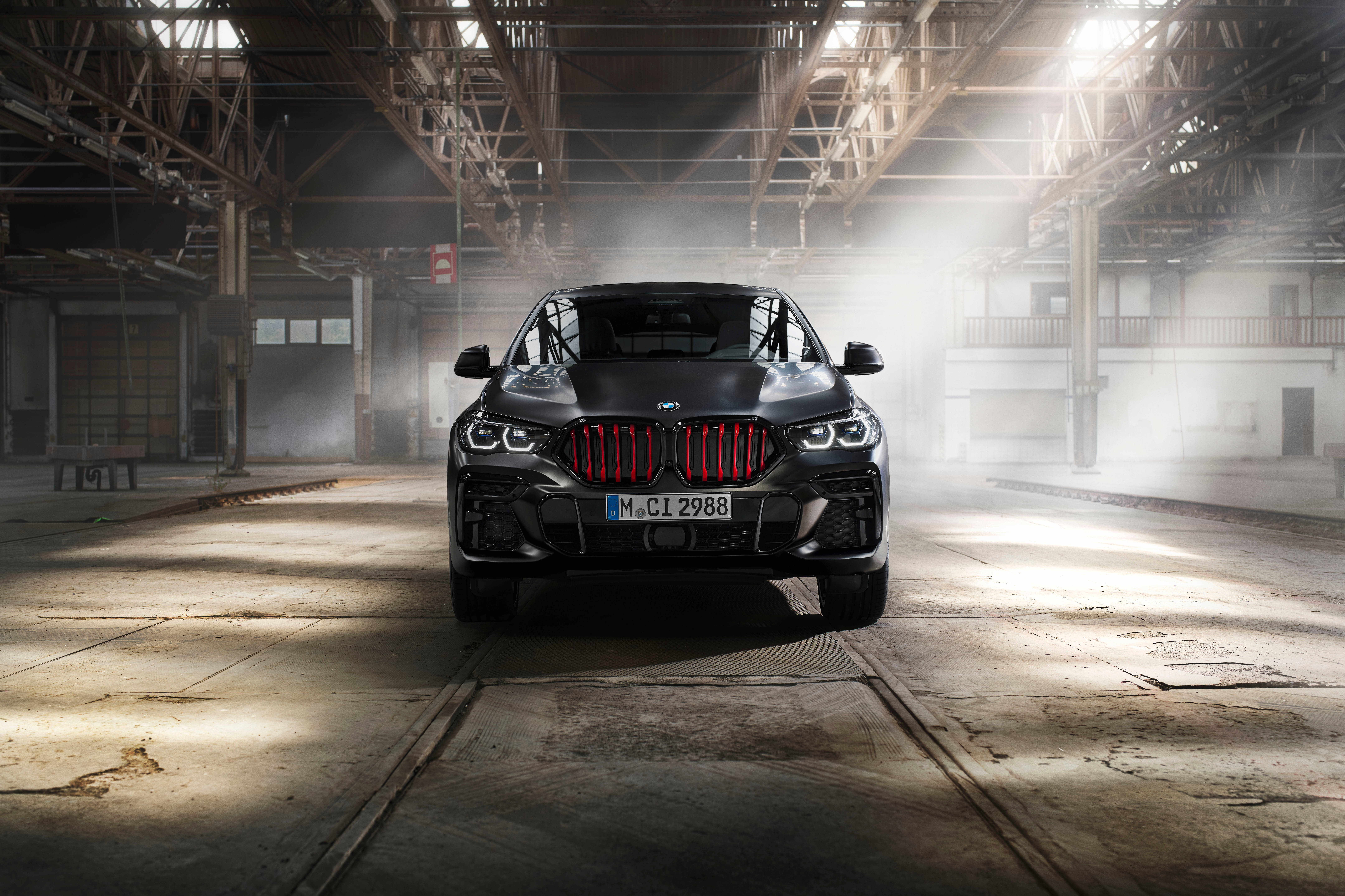 2021 黑色 BMW X6 前視圖 壁紙 — 一輛啞光黑色BMW X6 M Competition配以發光紅色格柵，戲劇性地矗立在灰塵滿佈的工業倉庫中，光線從上方照射。