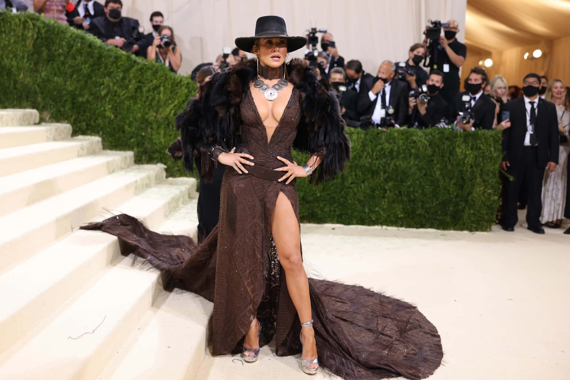 Rihanna 身穿棕色羽毛長袍和帽子，在樓梯上擺姿勢參加晚會。