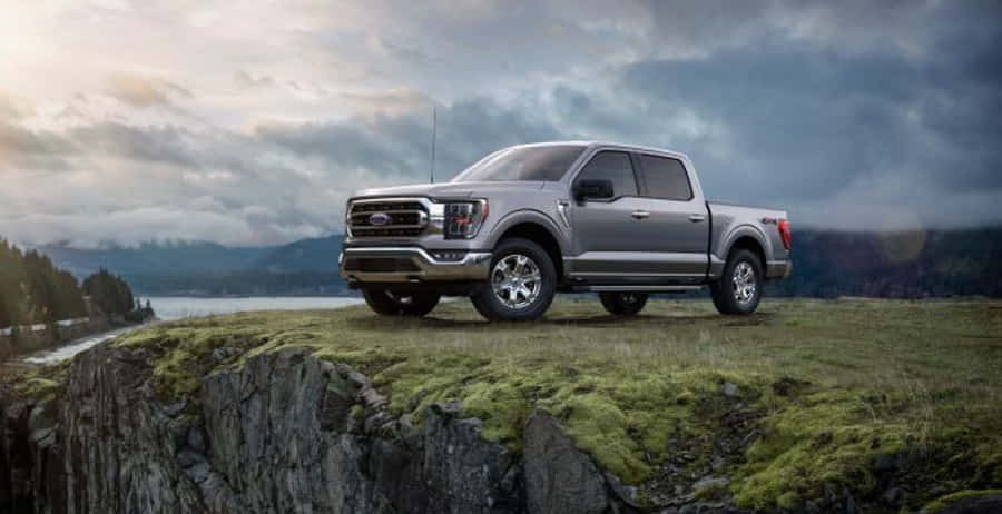 2021款灰色福特F-150皮卡攝影 壁紙 — 一架銀色福特F-150皮卡車停喺長滿苔蘚嘅懸崖上，俯瞰住霧氣瀰漫嘅湖泊同森林覆蓋嘅山脈，天空多雲。