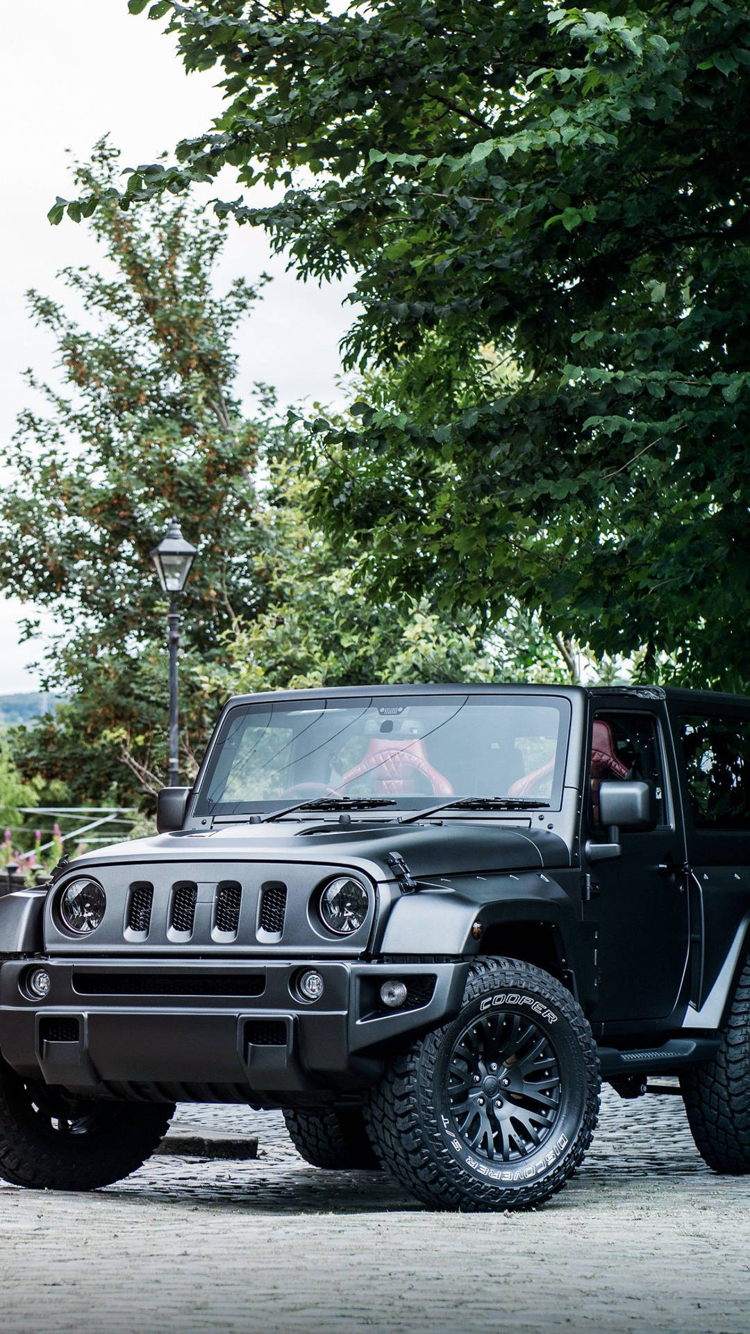 黑色Jeep Wrangler停泊在鵝卵石街道上，上方是茂密的樹木。