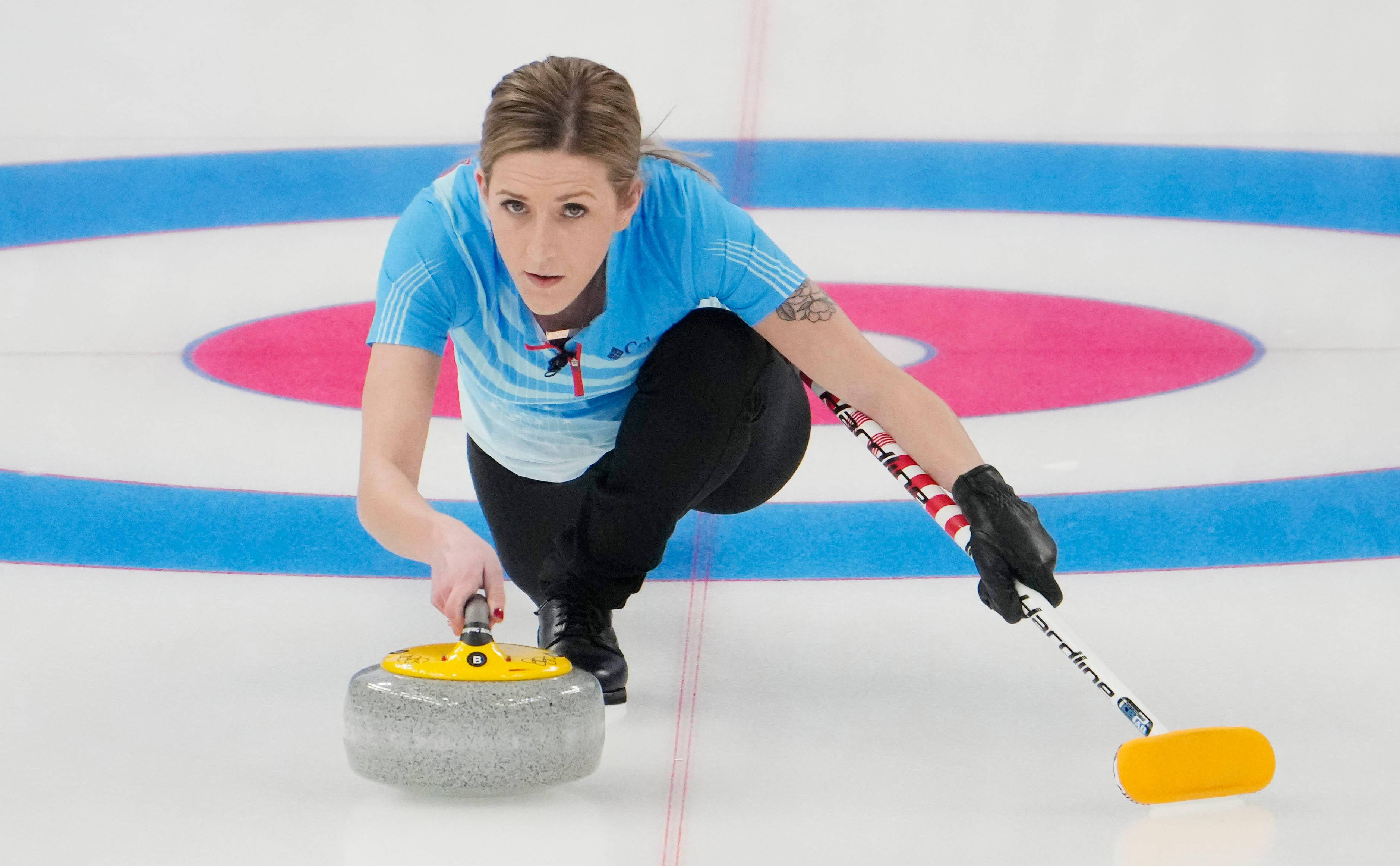 2022冬季奧運冰壺選手 Vicky Persinger 壁紙 — 一位專注的女性冰壺運動員身穿藍色球衣，用黃色手柄掃帚在冰面上滑動花崗岩石頭。