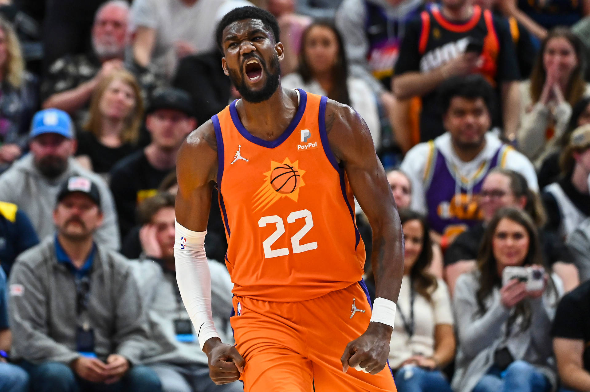 2022年NBA賽季德安德烈·艾頓鳳凰城太陽隊 壁紙 — 一名身穿橙色太陽隊球衣的籃球運動員在比賽中對著背景的人群激烈咆哮。