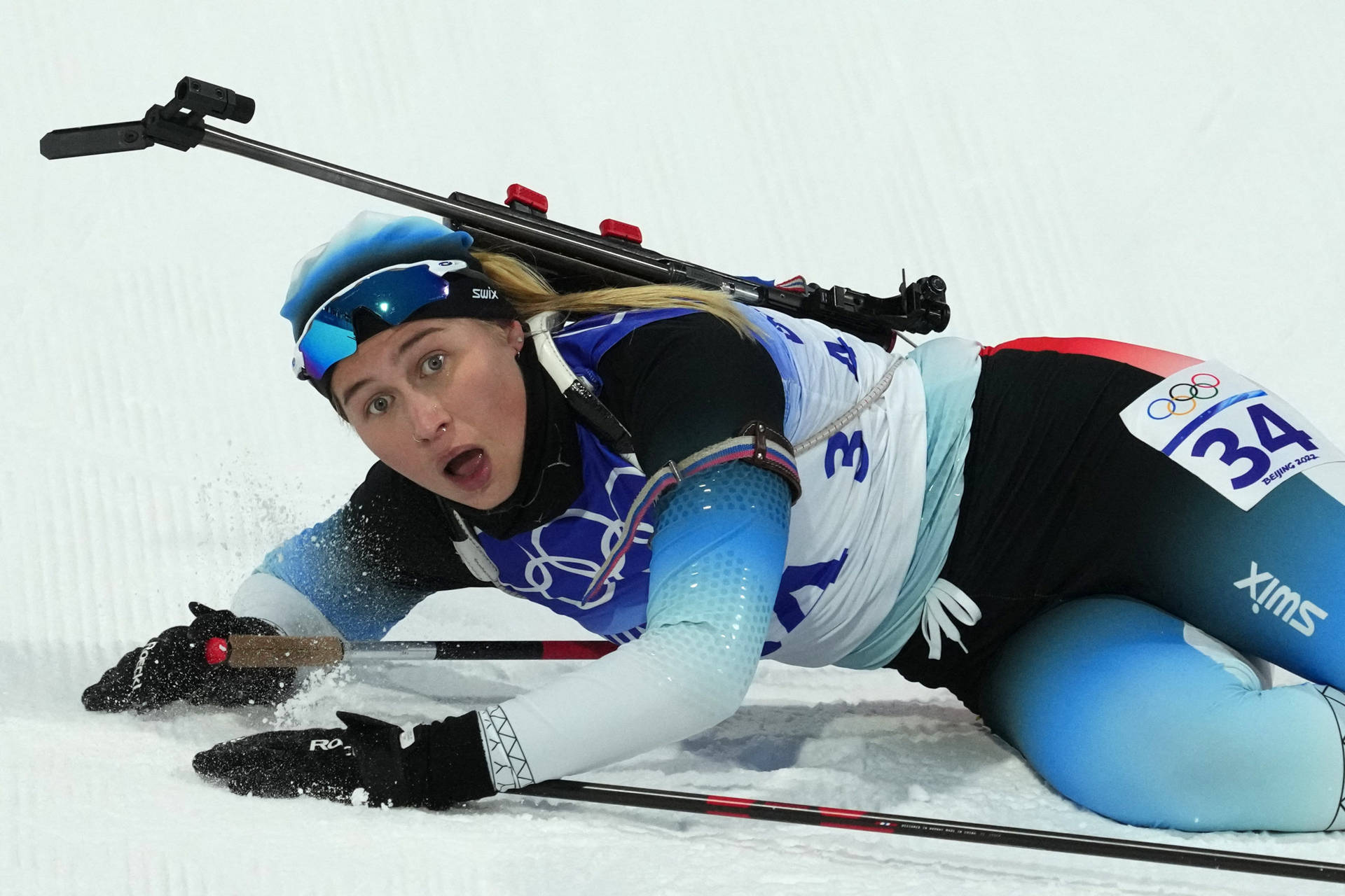 2022年冬季奧運會女子越野滑雪射擊運動員烏卡列克·阿斯特里·斯萊特馬克 壁紙 — 一位身穿藍白裝備的冬季兩項運動員在雪地地形上俯臥，比賽期間專注地瞄準步槍。