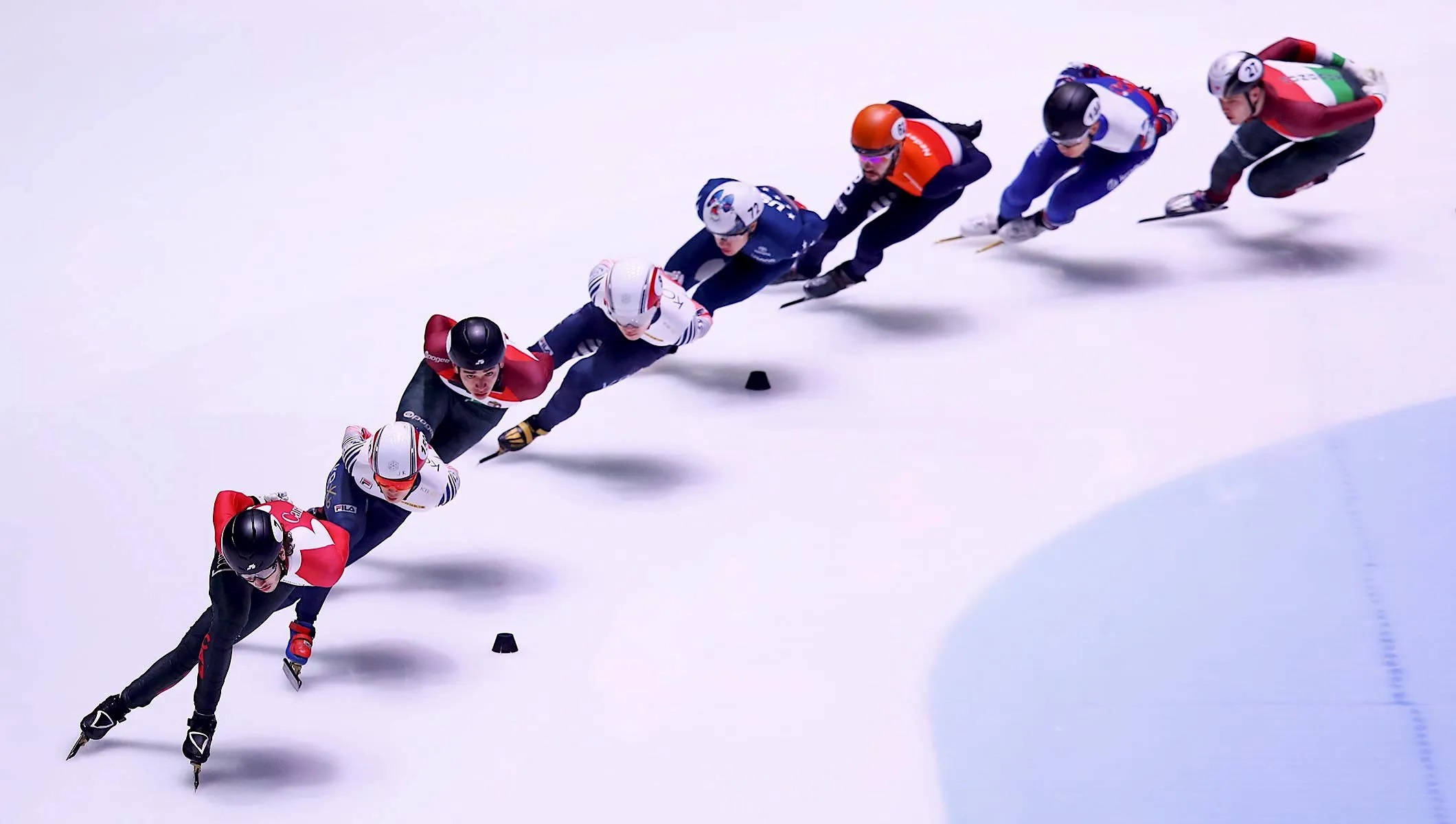 2022年冬季奧運短道速滑空中俯瞰 壁紙 — 速度滑冰選手在冰場上彎道傾身，進行激烈比賽，身穿色彩繽紛的制服。
