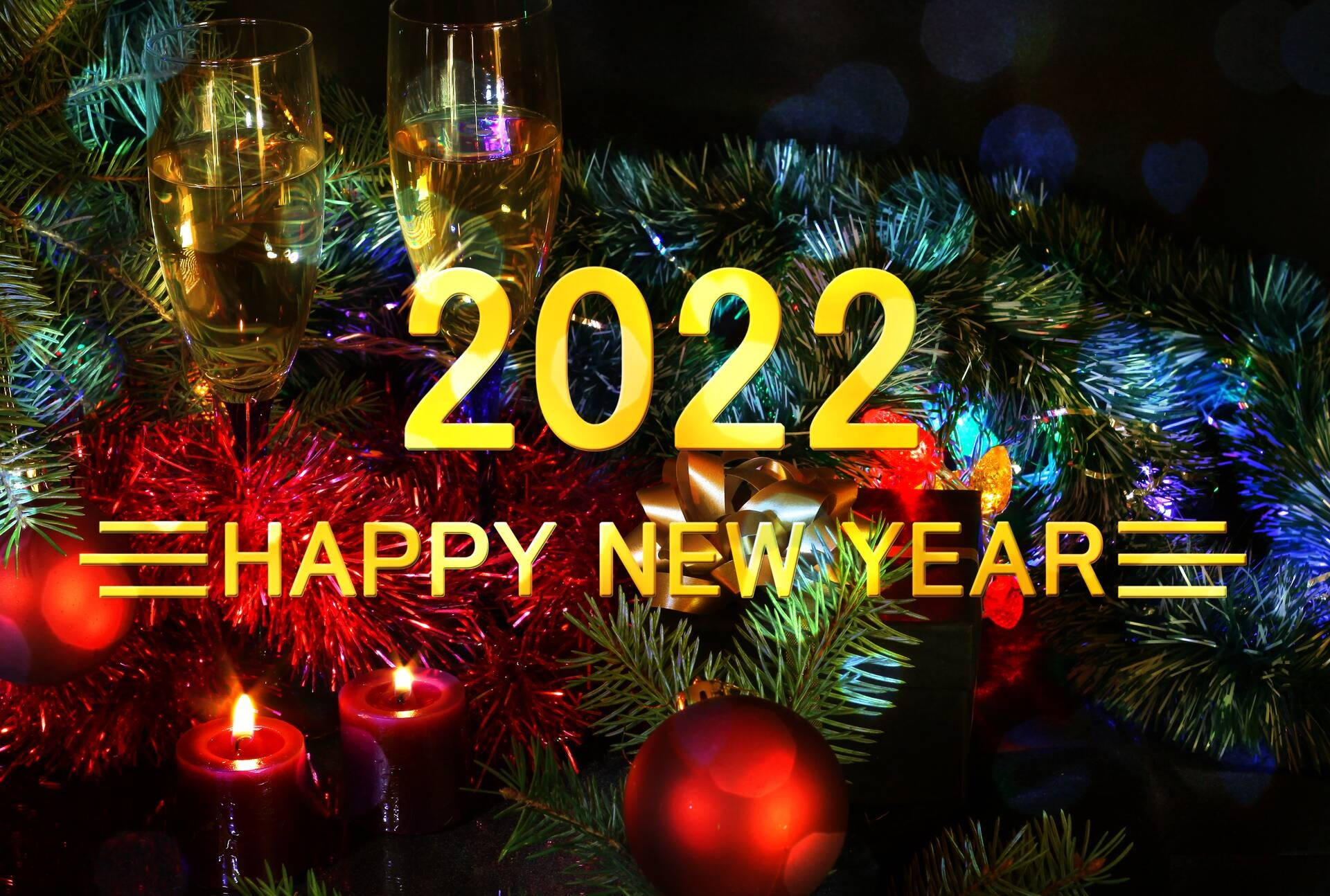 2022新年快樂聖誕樹壁紙 壁紙 — 金色嘅 '2022 HAPPY NEW YEAR' 文字喺黑暗散景背景上，喺節日松樹枝、蠟燭同香檳杯上面發光。