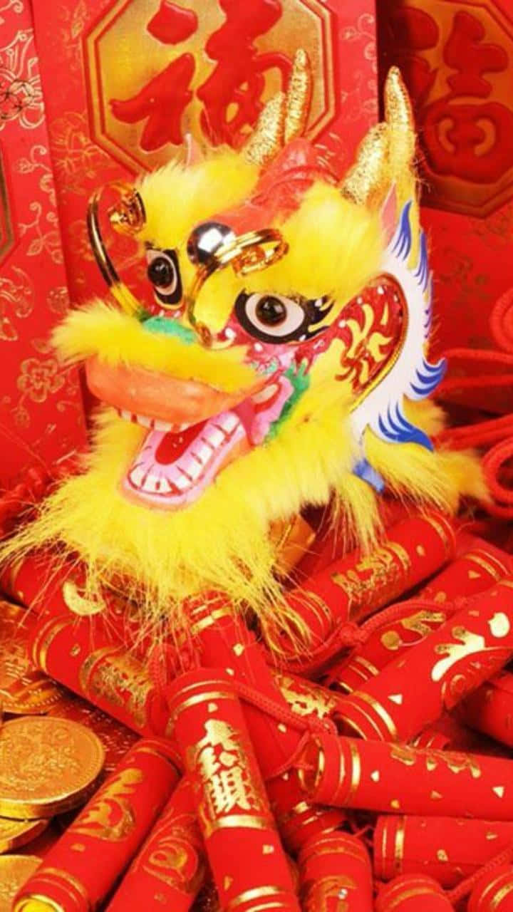 2022春節龍頭 壁紙 — 一個鮮黃色的舞獅頭，周圍環繞著紅色鞭炮和金幣，背景是喜慶的紅色。