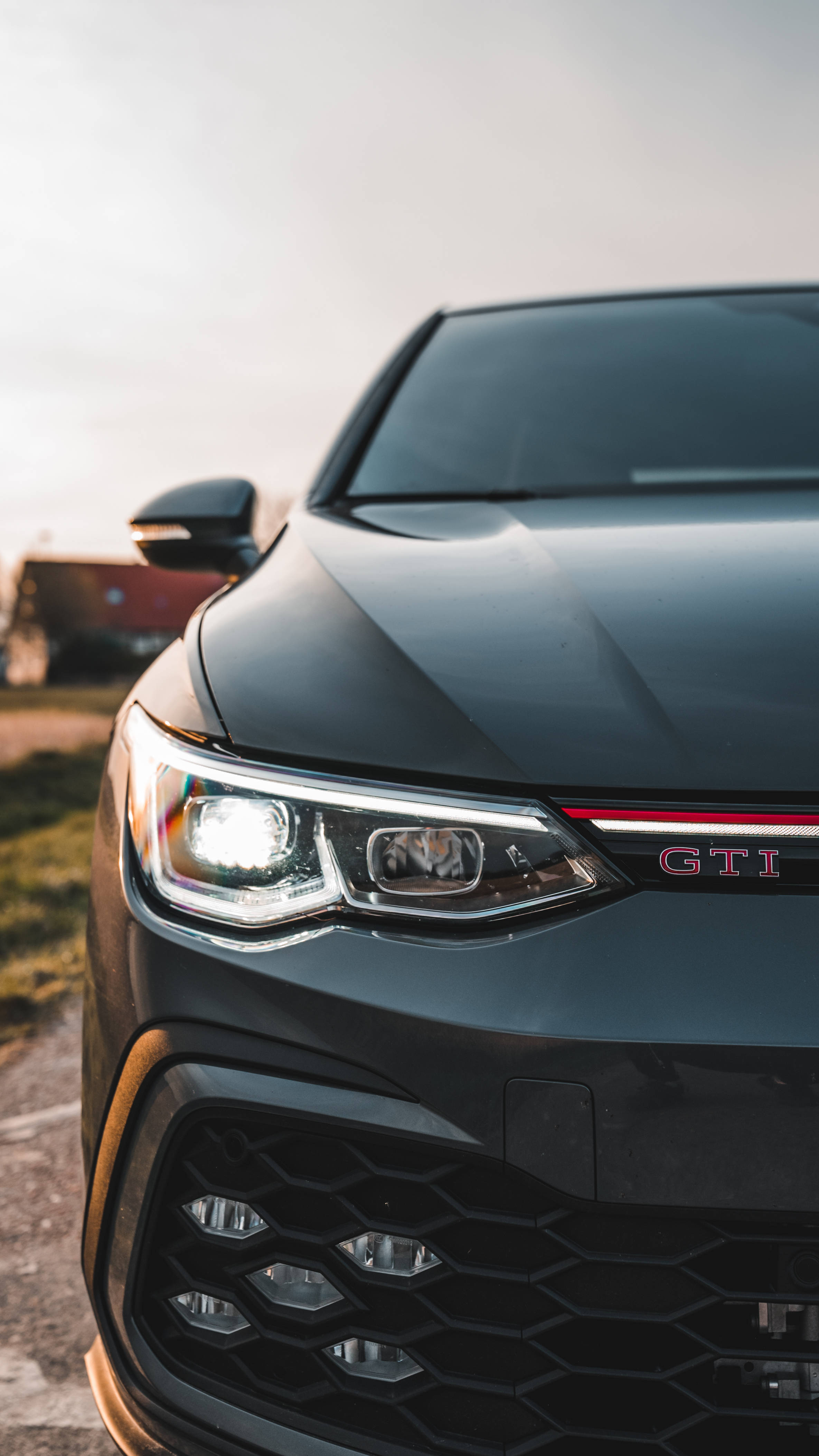 2022款 Volkswagen Golf GTI 黑色特寫 壁紙 — 黑色GTI汽車的車頭格柵和頭燈在柔和的金色日落光線下閃耀的特寫。
