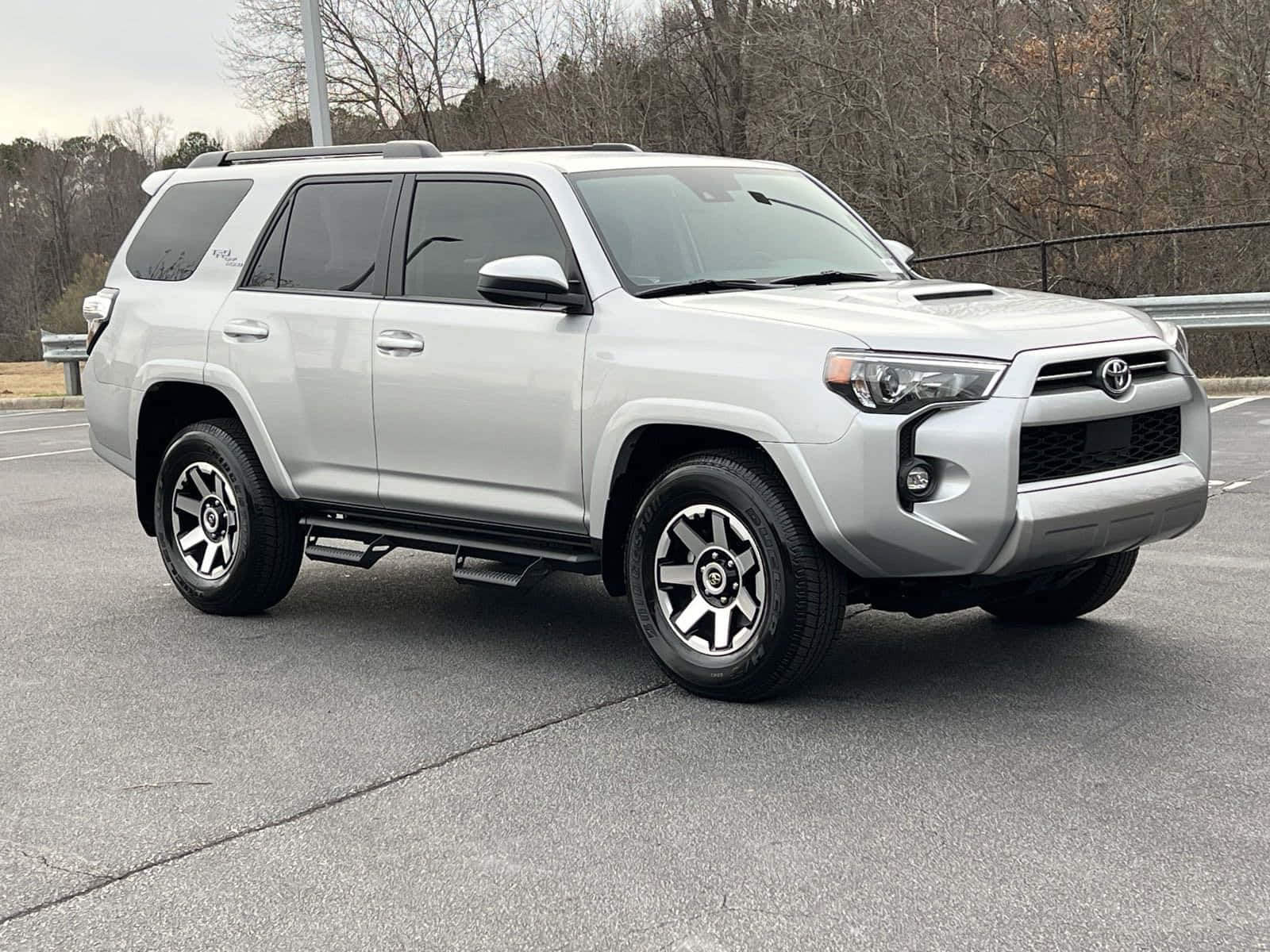 以2023款豐田4Runner留下深刻印象 壁紙 — 一架銀色豐田4Runner SUV停泊在一個有光禿樹木和陰天背景的停車場。