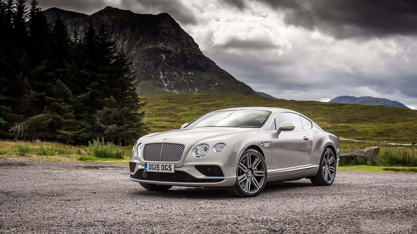2023款灰色賓利Continental GT背景圖 壁紙 — 一架時尚的銀色賓利 Continental GT 停泊在碎石路上，背景是戲劇性的山脈和烏雲。