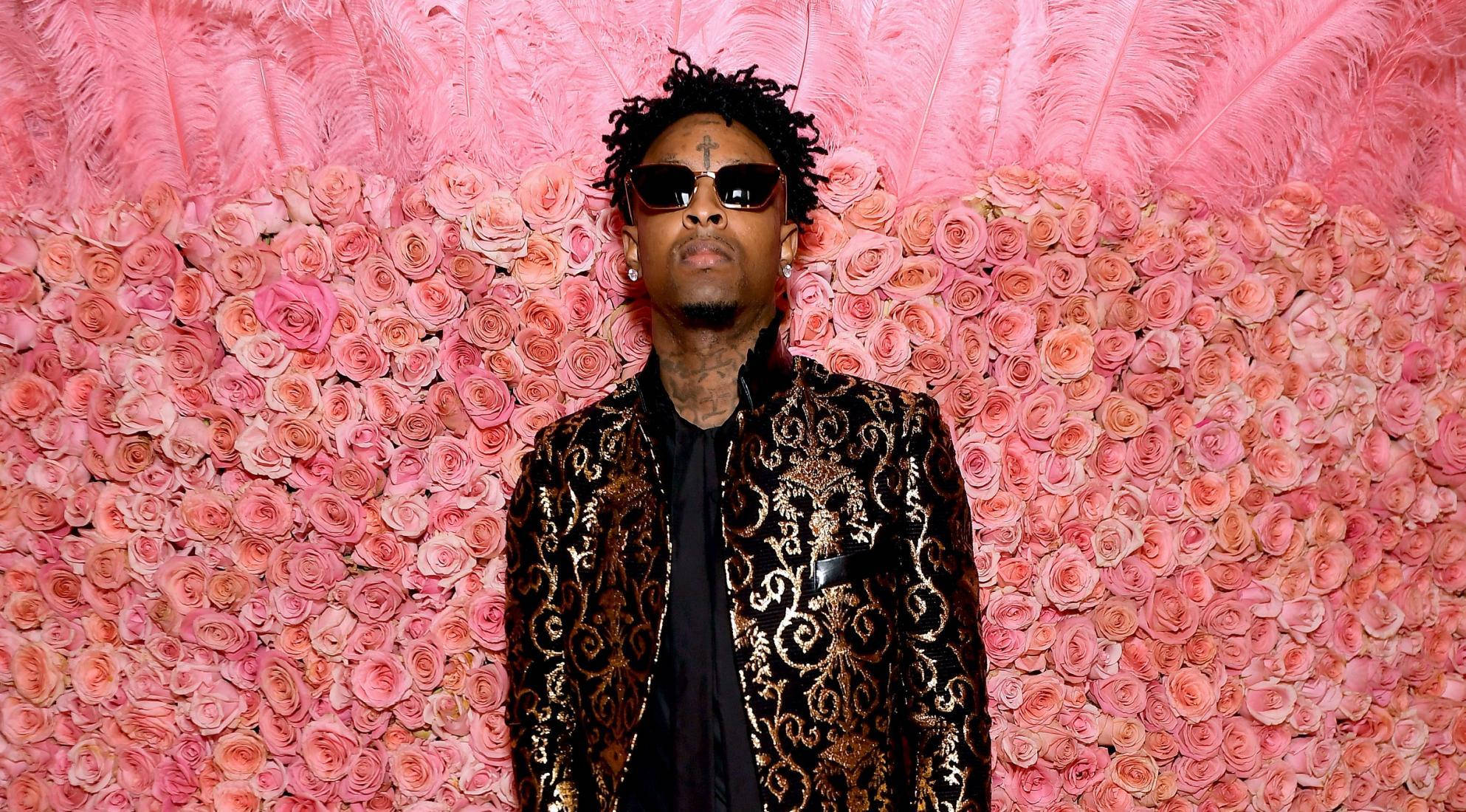 21 Savage 2019 梅特羅波利坦藝術博物館時裝晚宴 壁紙 — 一名戴著太陽眼鏡和華麗外套的男子站在粉紅玫瑰和羽毛牆前。