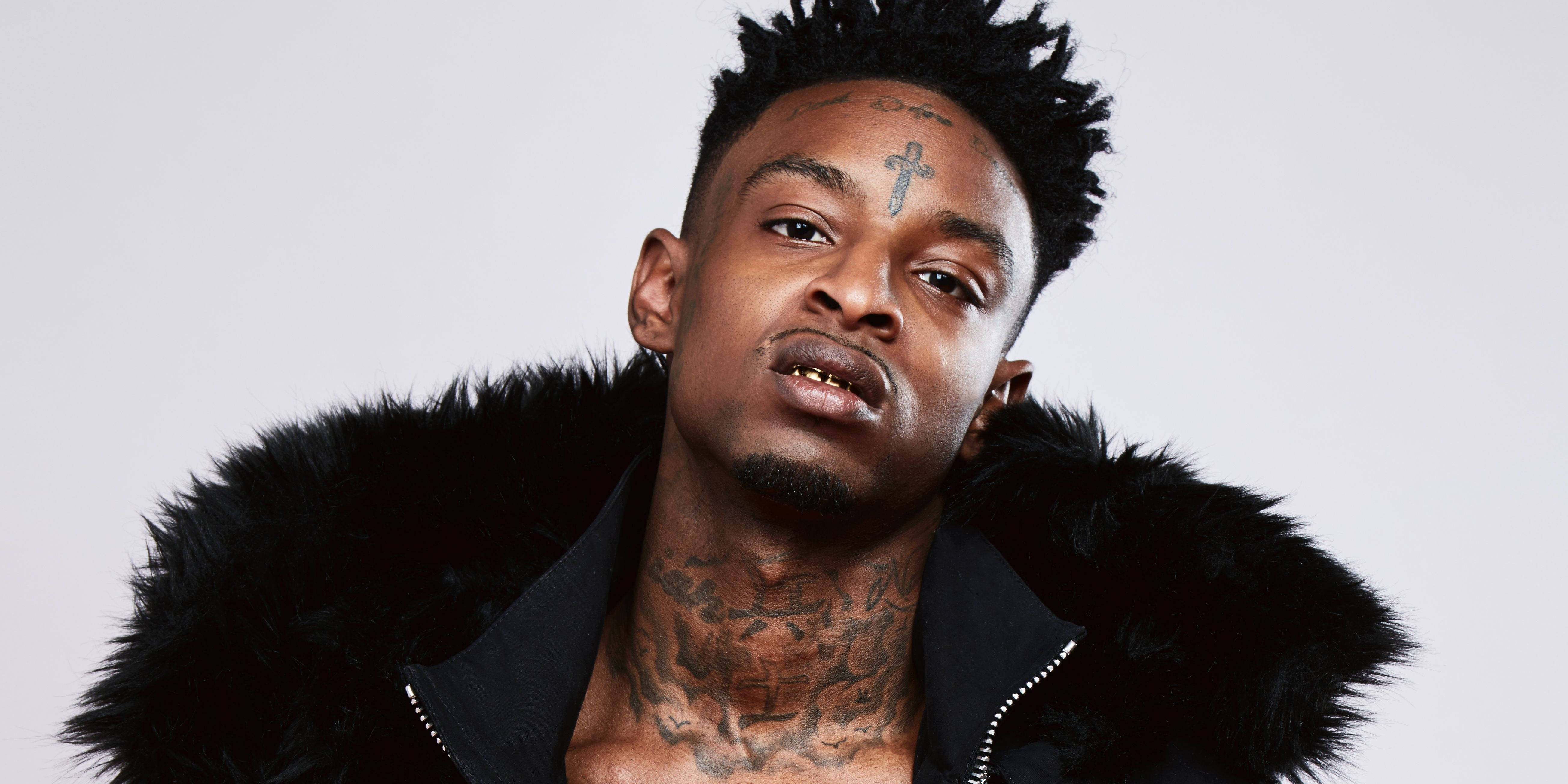 21 Savage 假毛皮外套 壁紙 — 一個有紋身、穿著黑色毛領外套的男人，在純白背景下強烈凝視。
