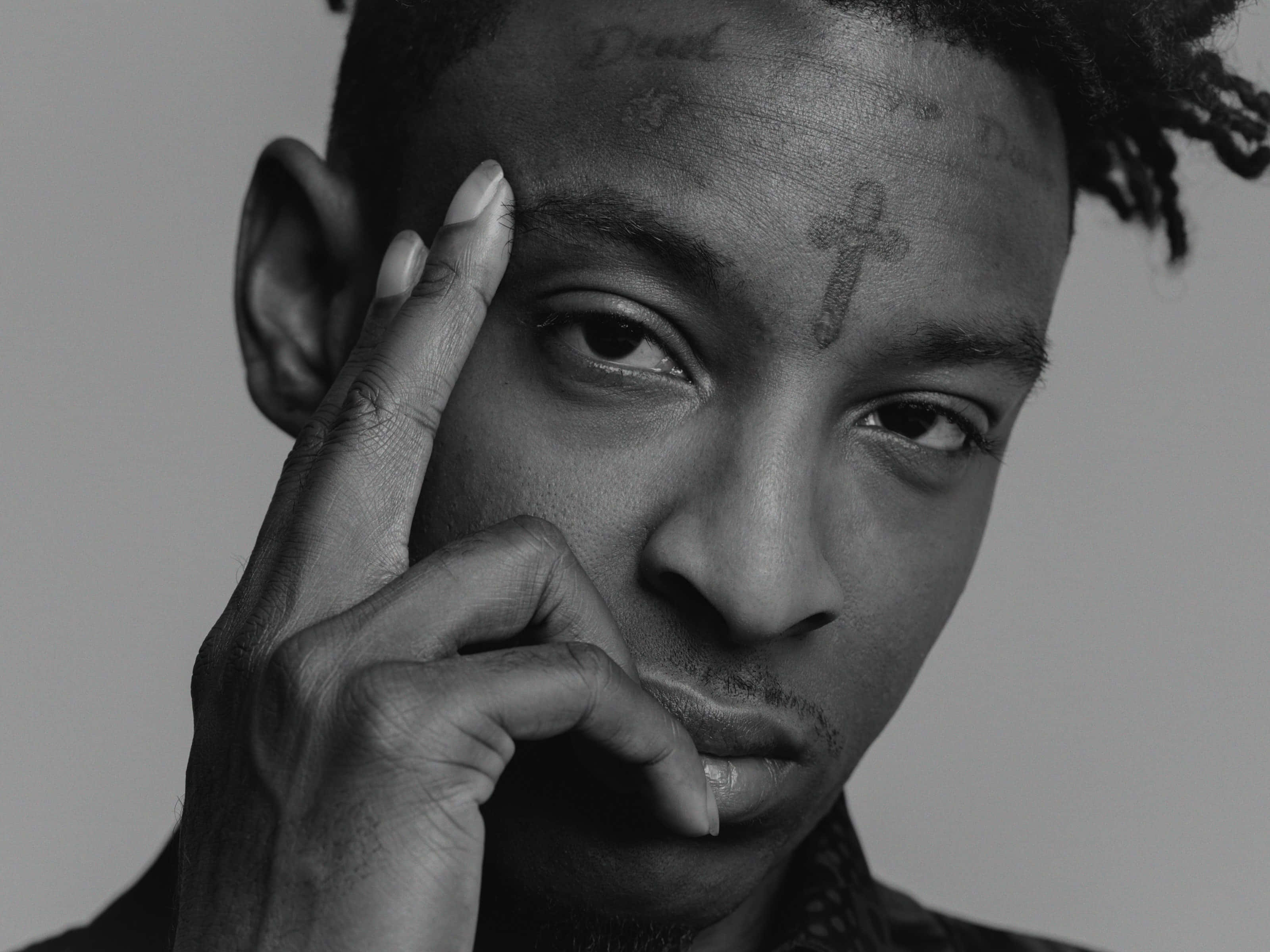 21 Savage 准備征服音樂界 壁紙 — 一個黑白肖像，男人額頭上有紋身，手放在臉附近。