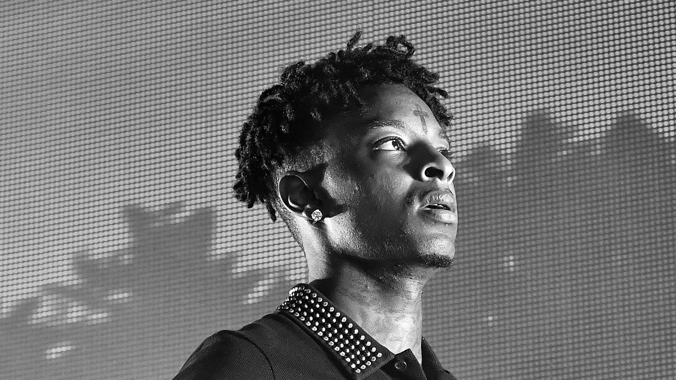 21 Savage 在 Cellairis 室外劇場演出 壁紙 — 一個黑白肖像，年輕男子擁有紋理頭髮和鉚釘項圈，在像素化屏幕背景下向上凝視。