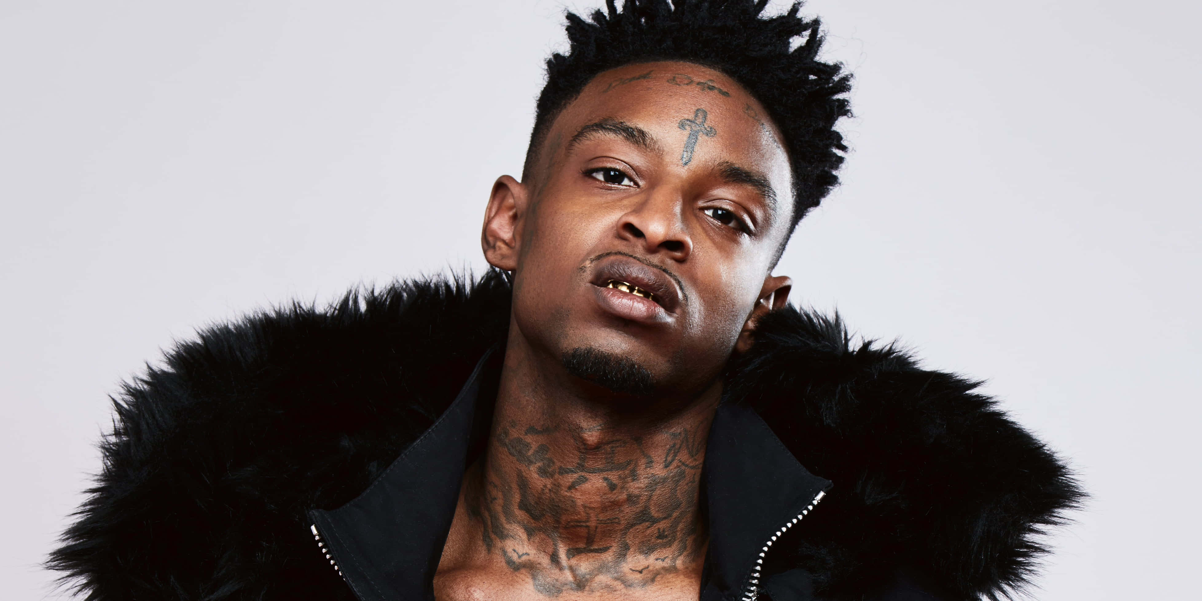 21 Savage 在演唱會上表演 壁紙 — 一個有紋身、穿著黑色毛領外套的男人，在純白色背景下強烈地凝視。