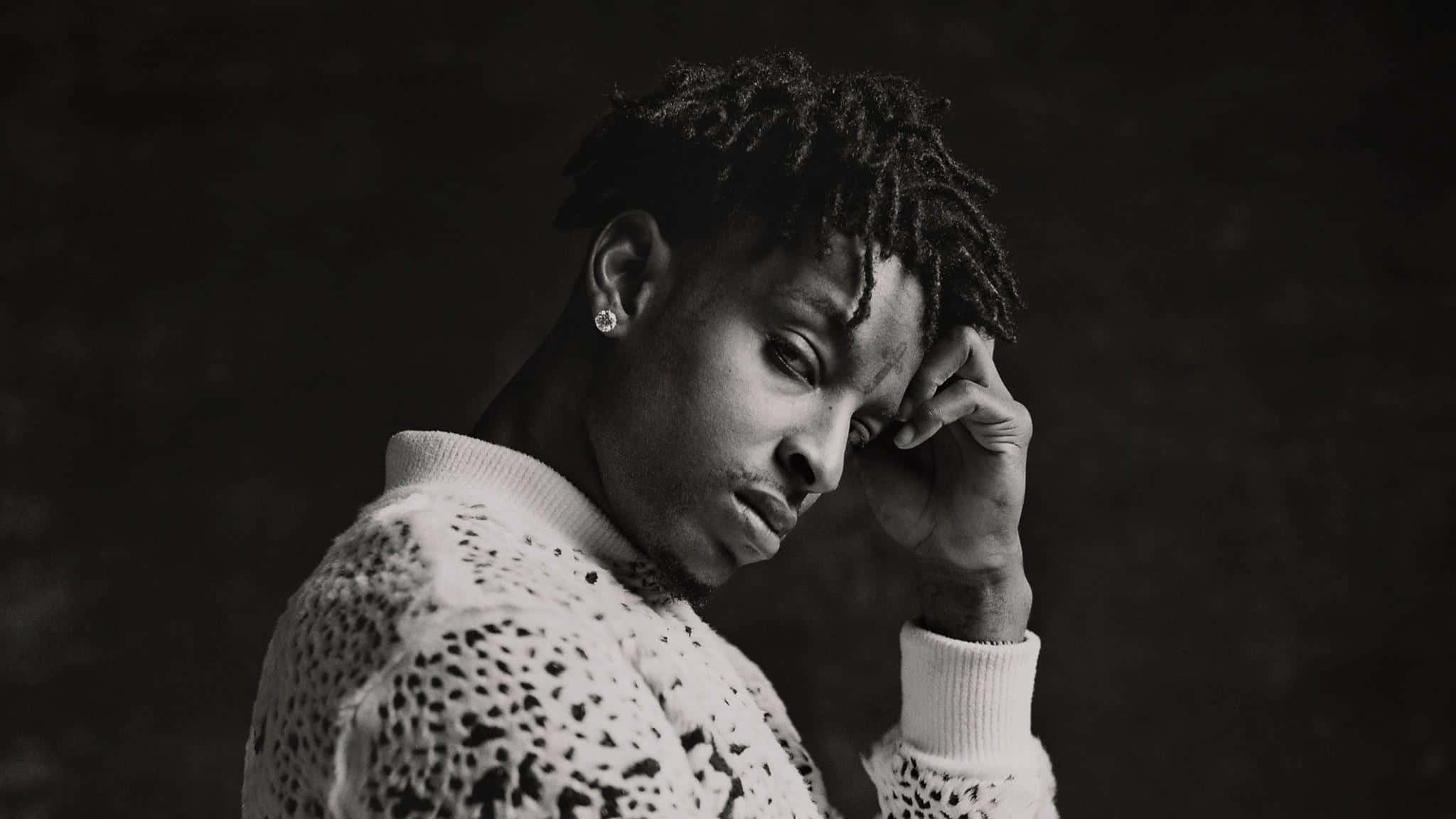 21 Savage — 阿爾特嘻哈界冉冉升起的新星 壁紙 — 一個留著辮子頭的男人以沉思姿態觸碰額頭的黑白肖像。