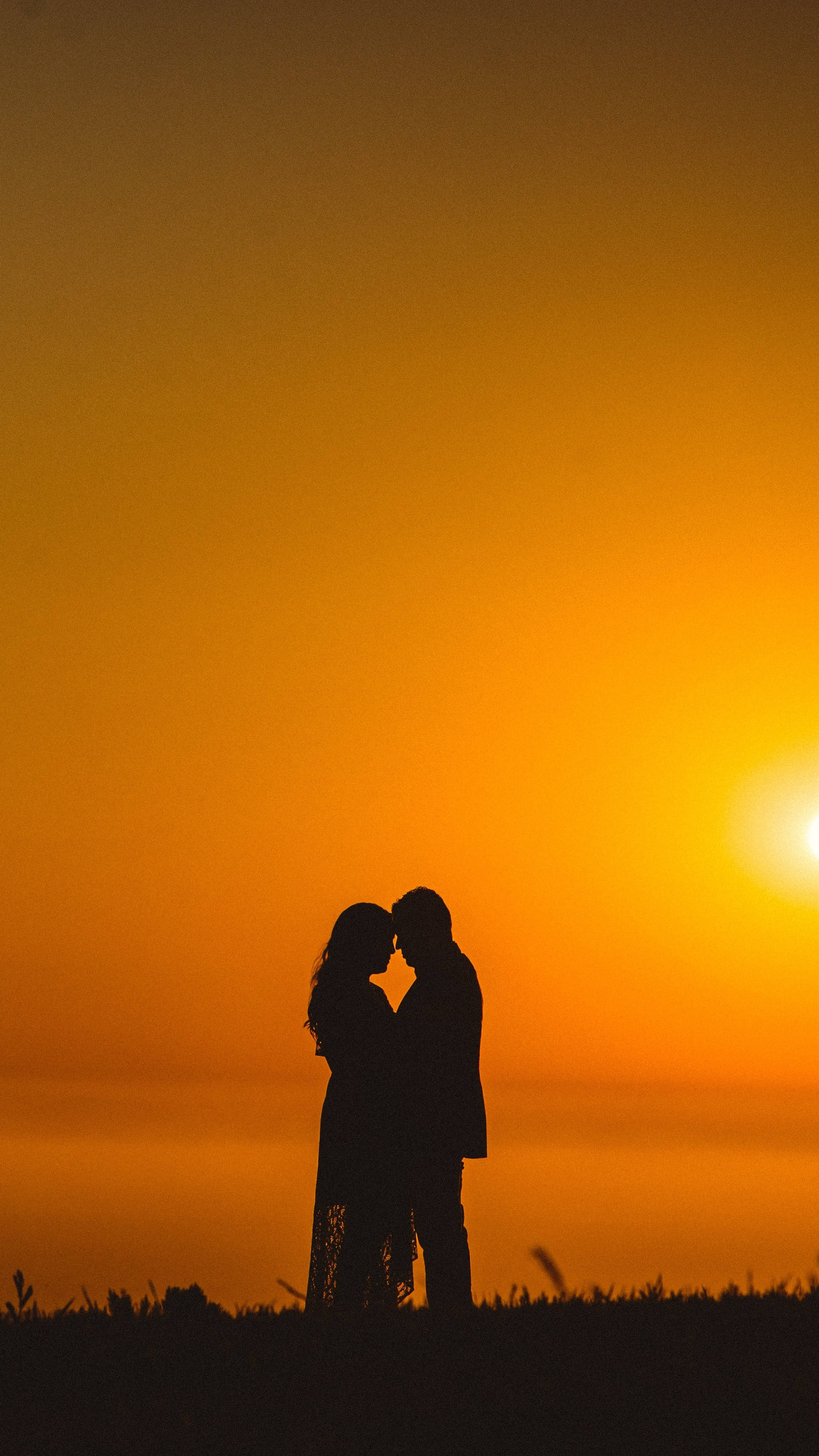 情侶剪影 2160x3840 壁紙 — 一對情侶在火紅橙色夕陽天空下擁抱的浪漫剪影。