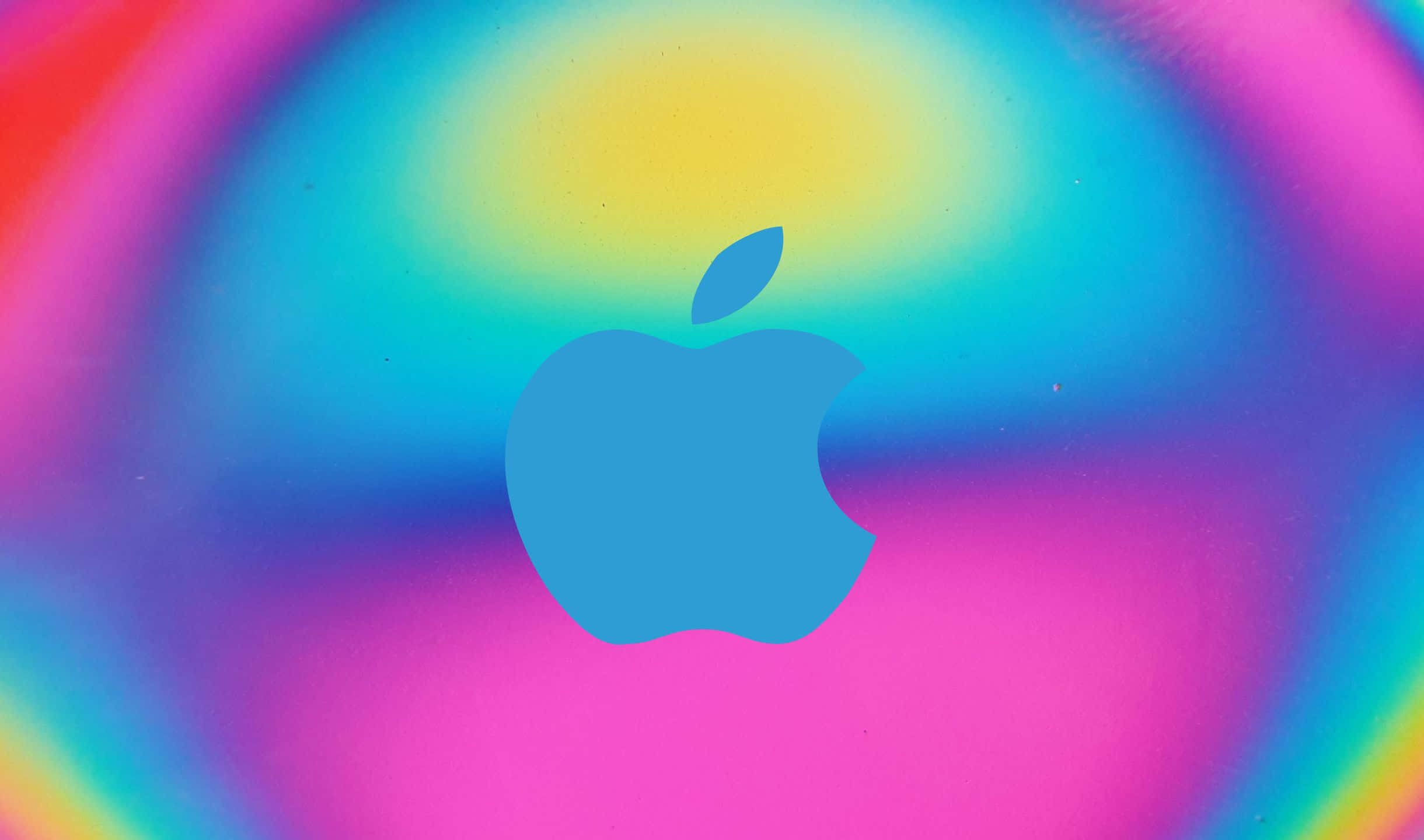 2440x1440 Apple 標誌光暈背景 壁紙 — 一個藍色Apple標誌居中於充滿活力的彩虹漸變背景上，帶有柔和模糊的邊緣。