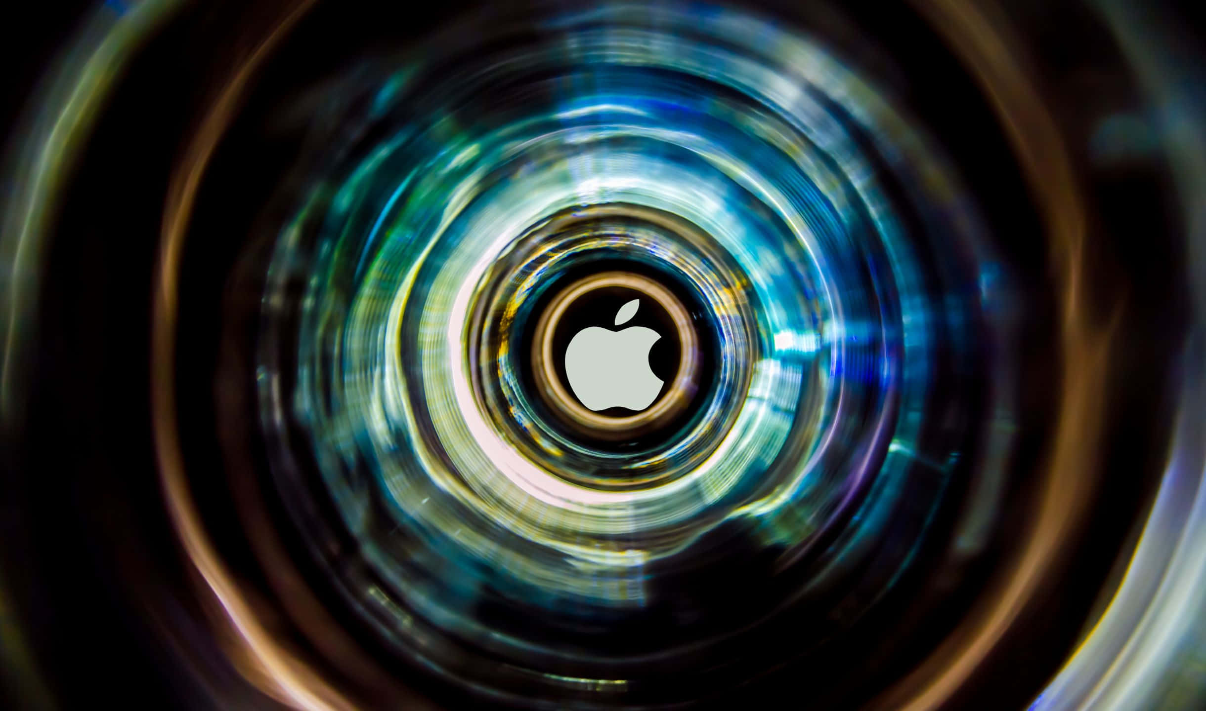 2440x1440 蘋果標誌於鏡頭背景 壁紙 — 一個發光的Apple標誌，位於充滿活力的藍色和金色光線漩渦隧道中央。