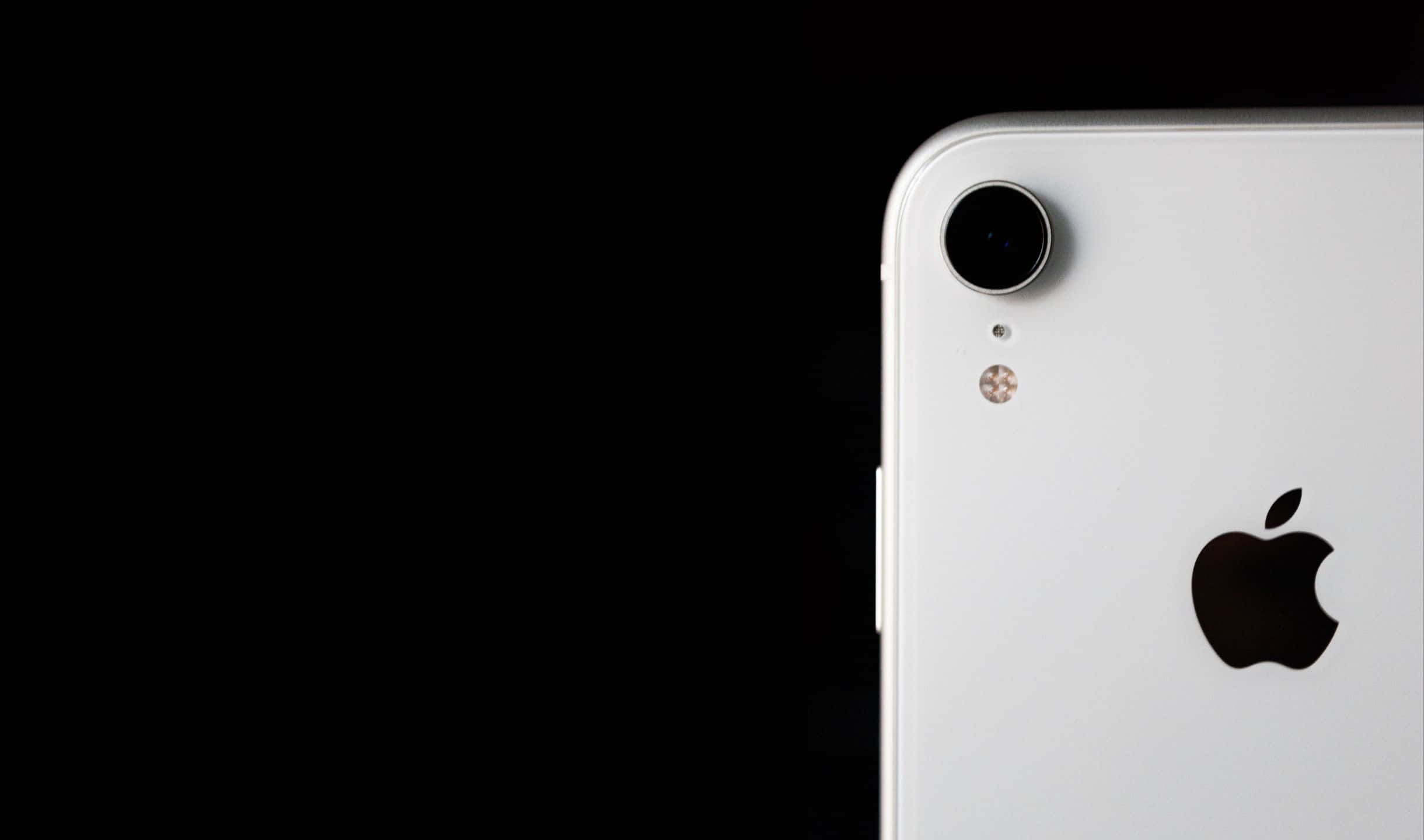 2440x1440 蘋果設備背景 壁紙 — 白色iPhone XR背面角落的特寫，在純黑背景下突出其相機和Apple標誌。