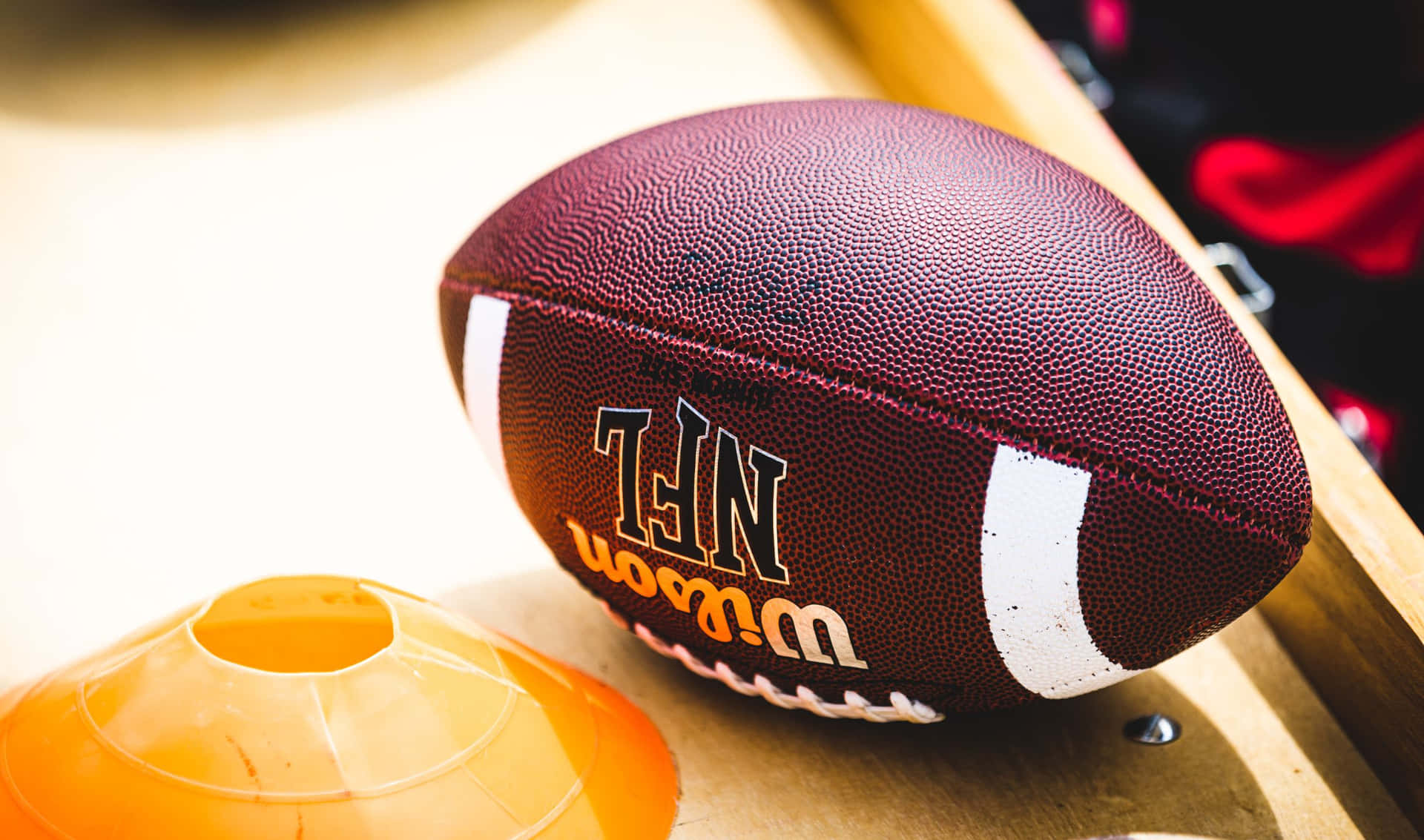 木質表面上的栗色NFL足球和橙色訓練錐體。