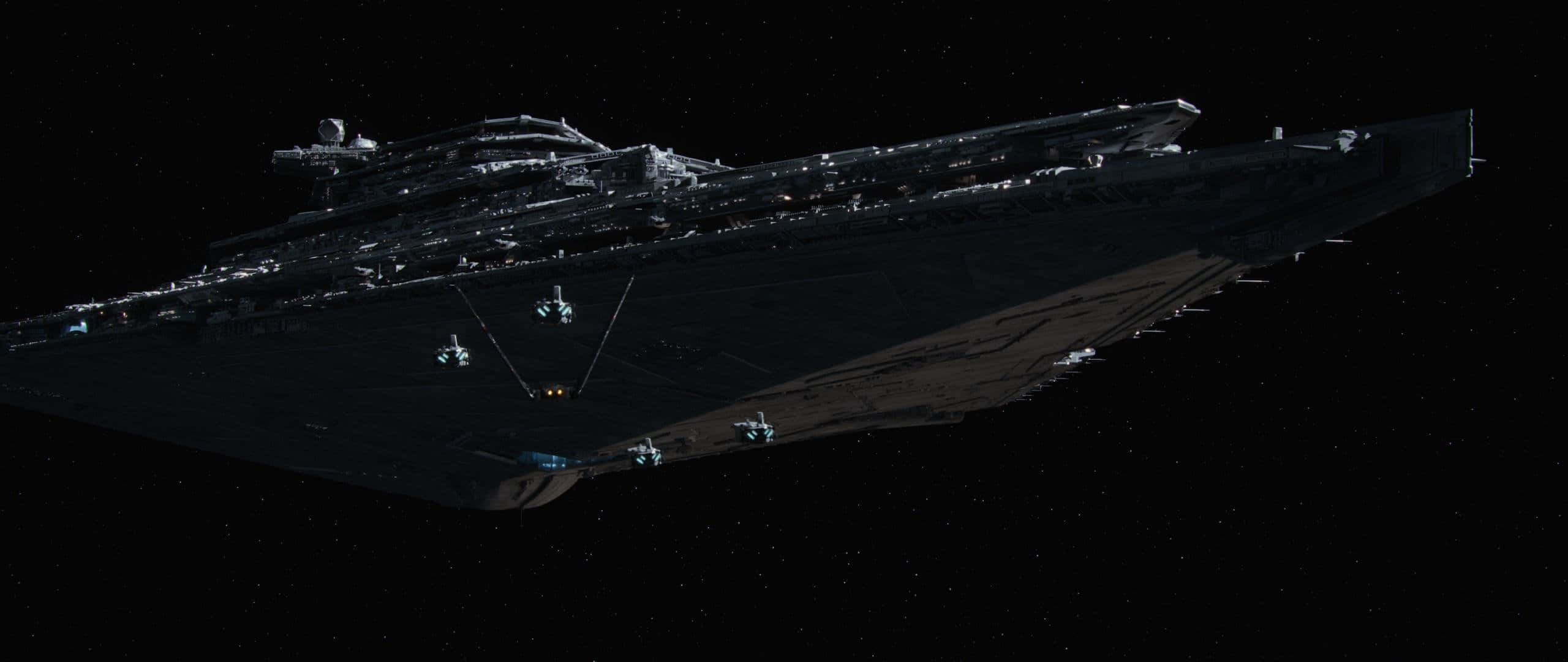 星際大戰 2560 x 1080 飛船 壁紙 — 一艘巨大的帝國星際驅逐艦在深空中若隱若現，小型星際戰鬥機護航，背景是無數的星星。
