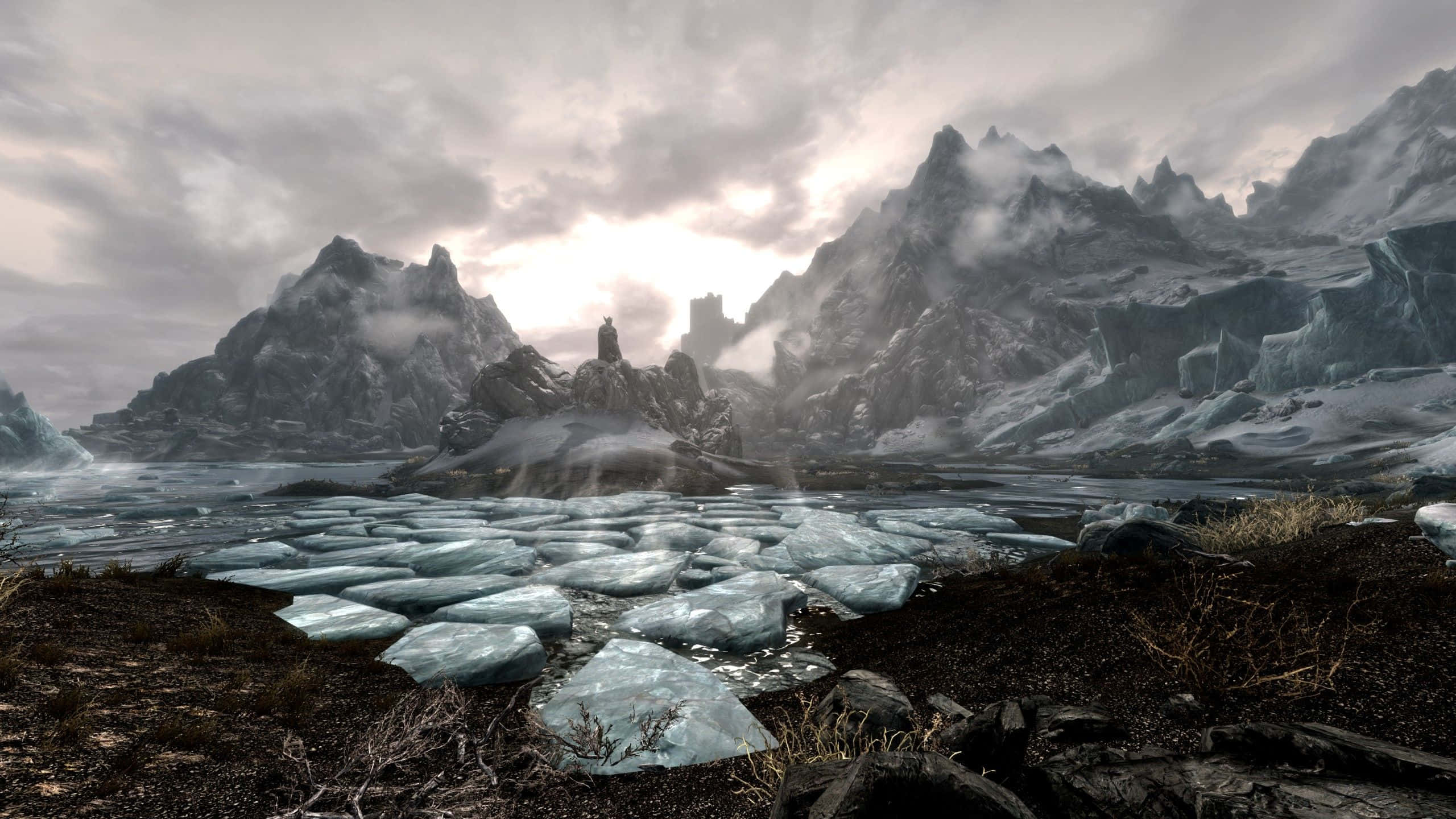 2560 X 1440 天際：冬季冰封湖景 壁紙 — 一個孤獨的身影站在崎嶇的浮冰上，身處荒涼的冰封山谷，四周被高聳的雪山環繞，天空多雲。
