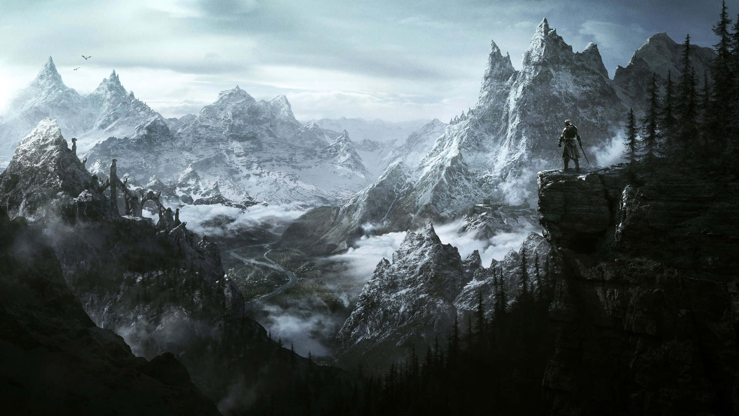 2560 X 1440 雪山風景 - 遊戲《上古卷軸V：天際》 壁紙 — 一位孤獨的戰士站在白雪覆蓋的山頂上，俯瞰著霧氣瀰漫的山谷，下方有鋸齒狀的山峰和古老的廢墟。
