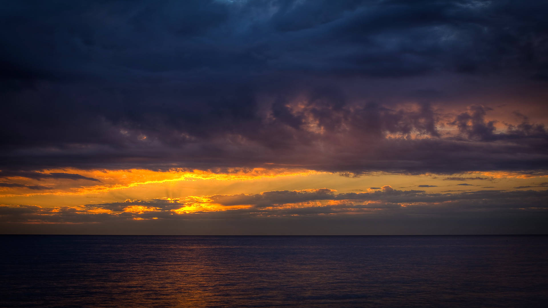 戲劇性的日落，橙色光線穿透烏雲，照耀平靜的海面。