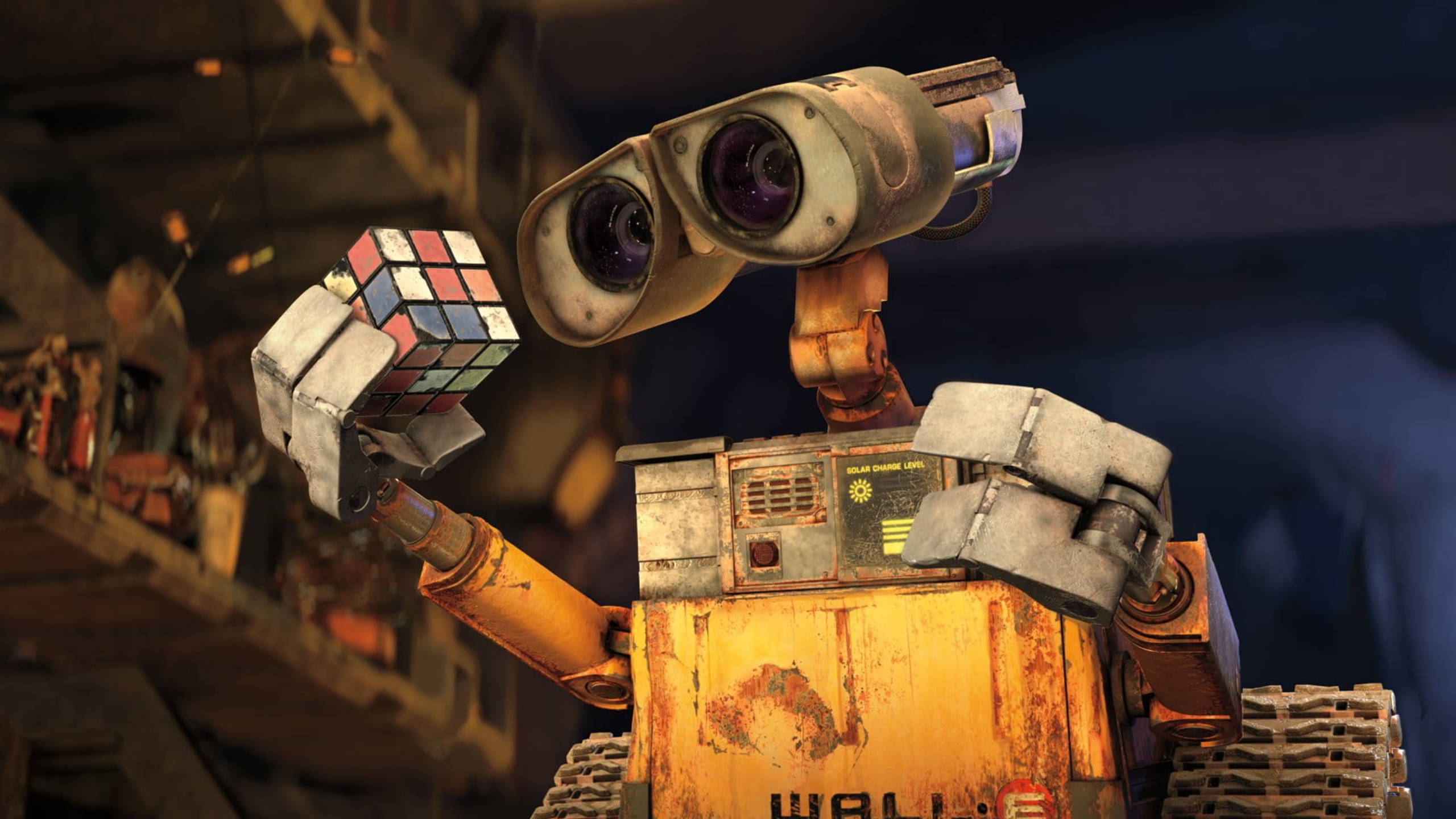 2560x1440 迪士尼《 WALL·E 》 壁紙 — 一個生鏽的黃色機械人，有著巨大的雙筒望遠鏡眼睛，在雜亂的工作室裡拿著一個已解開的扭計骰。