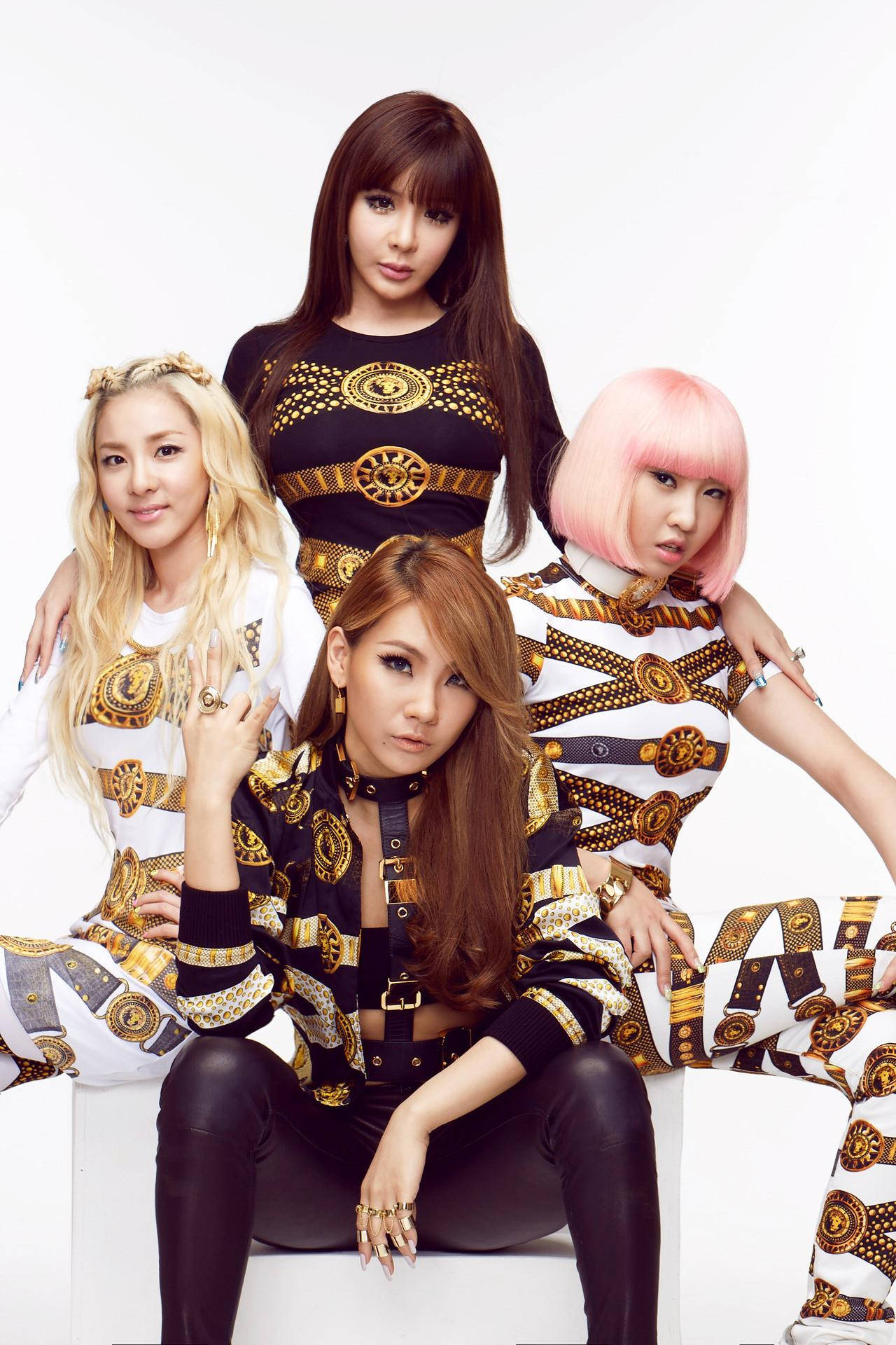 2NE1 穿金色服裝 壁紙 — 四位時尚女性身穿大膽的金色和黑色圖案服裝，在純白背景前自信地擺姿勢。