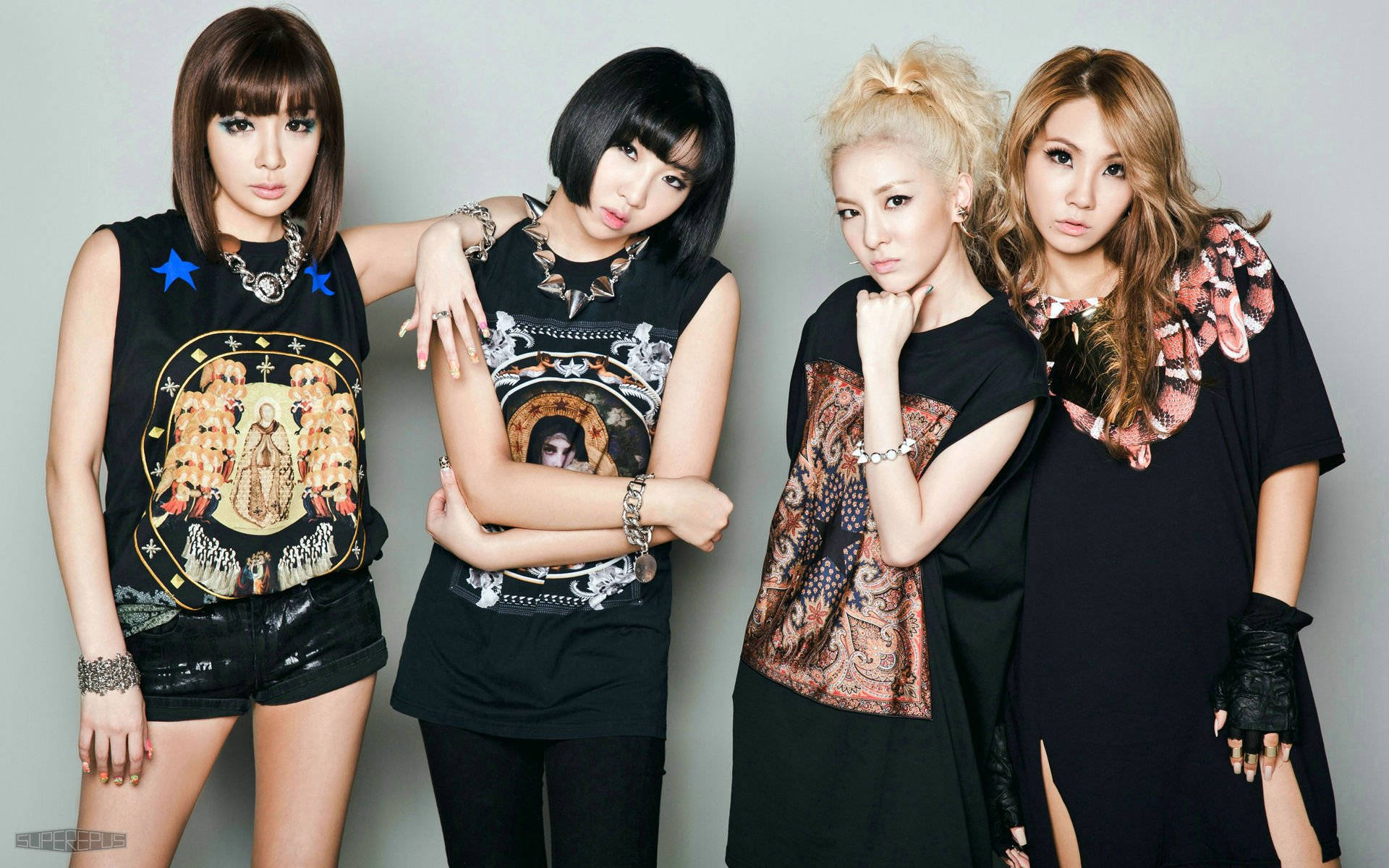 2NE1 韓國流行嘻哈女團 壁紙 — 四位時尚女性自信地擺姿勢，穿著前衛的黑色服裝，帶有醒目的圖案印花，背景是純灰色攝影棚。