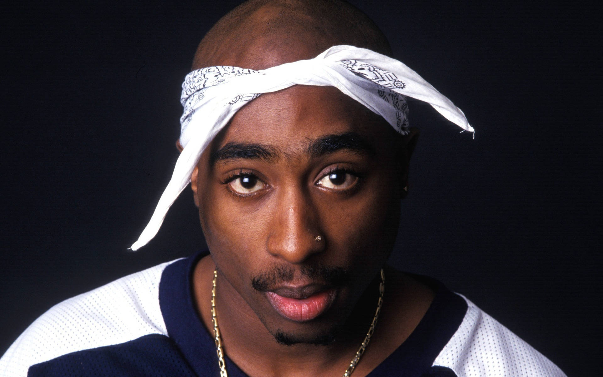 2Pac戴白色頭巾 壁紙 — Tupac Shakur 嘅肖像，佢戴住白色頭巾同金鏈，喺黑暗背景下專注咁望住鏡頭。