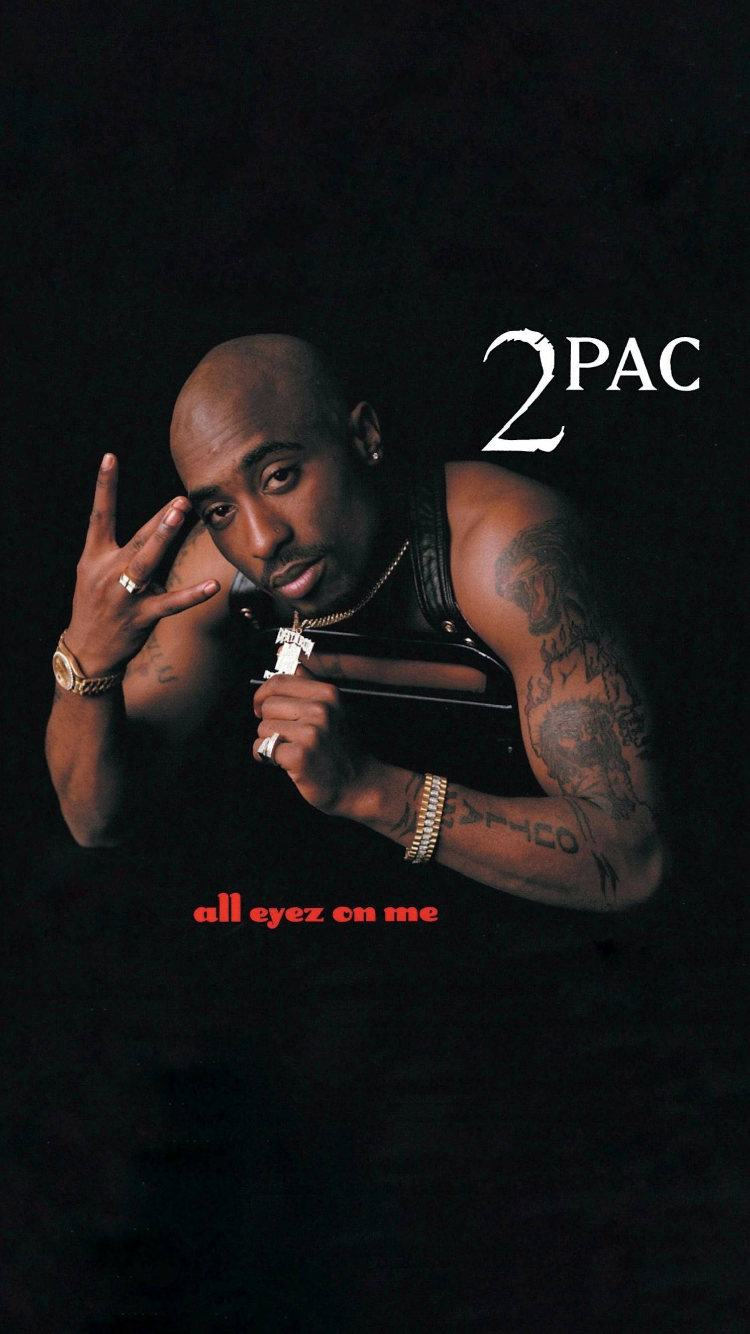 2Pac手寫W字 壁紙 — Tupac Shakur 凝視觀眾，手持帶有 '2PAC' 和 'all eyez on me' 文字的槍，背景為黑色。
