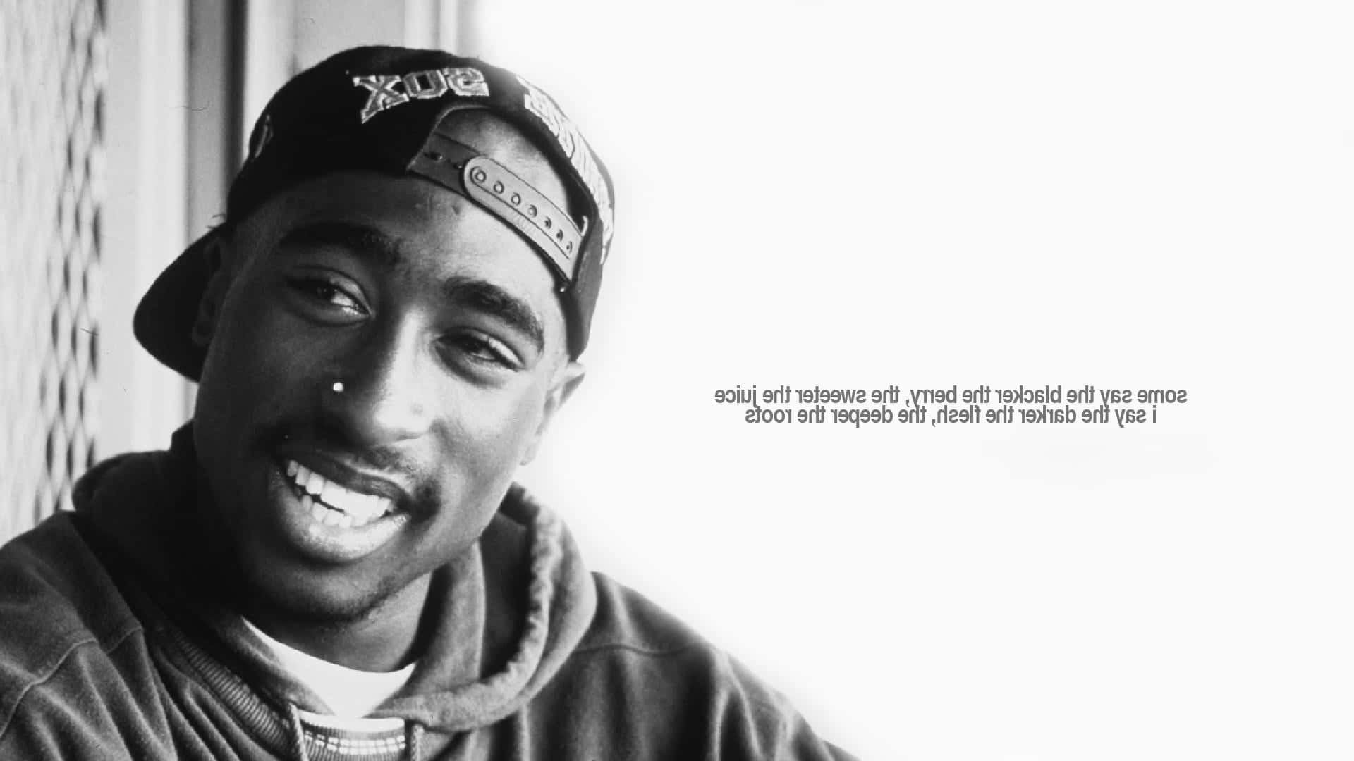 Tupac Shakur在黑白照片中微笑，戴著帽子和連帽衫，旁邊有歌詞文字。