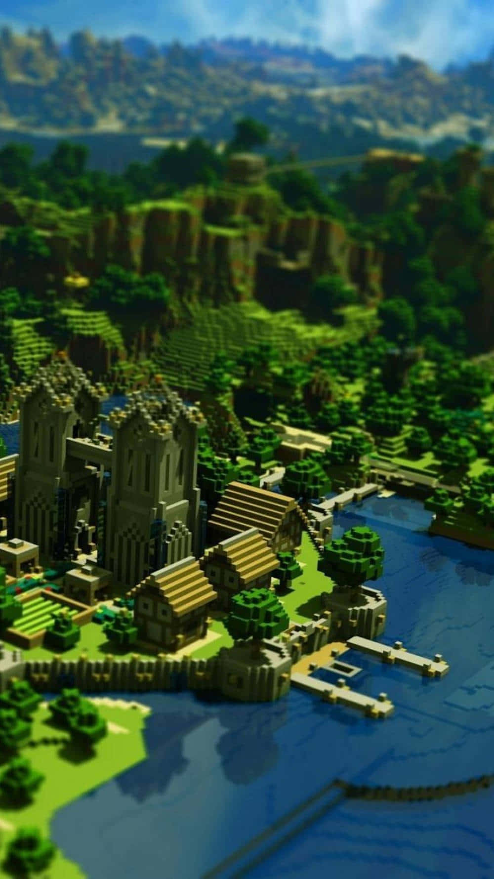 河畔城堡像素3 Minecraft背景 壁紙 — 一個充滿活力的像素化Minecraft村莊坐落在河邊，擁有茂密的綠色山丘和遠處的山脈，在明亮的藍天下。