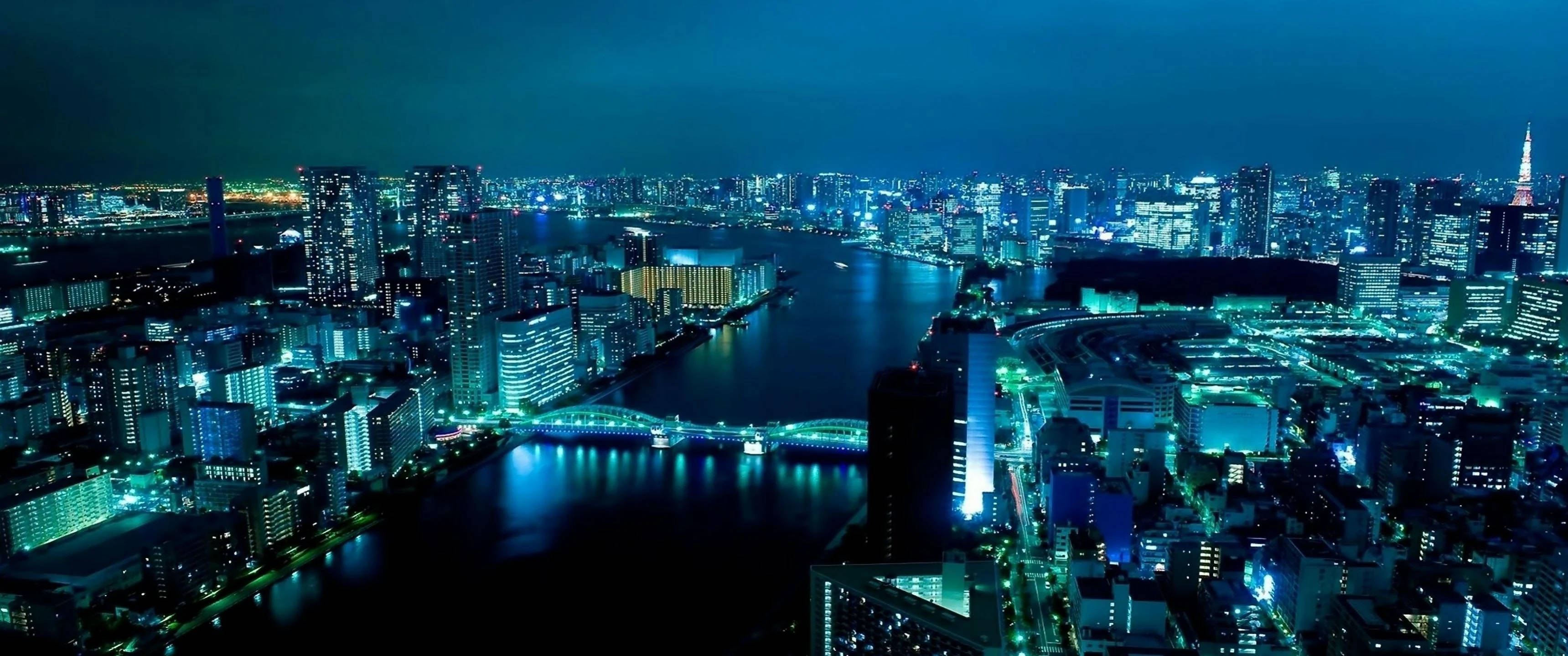 3440x1440 東京夜景 壁紙 — 東京夜景鳥瞰圖，摩天大樓閃爍，河流在黑暗天空下反射霓虹燈光。
