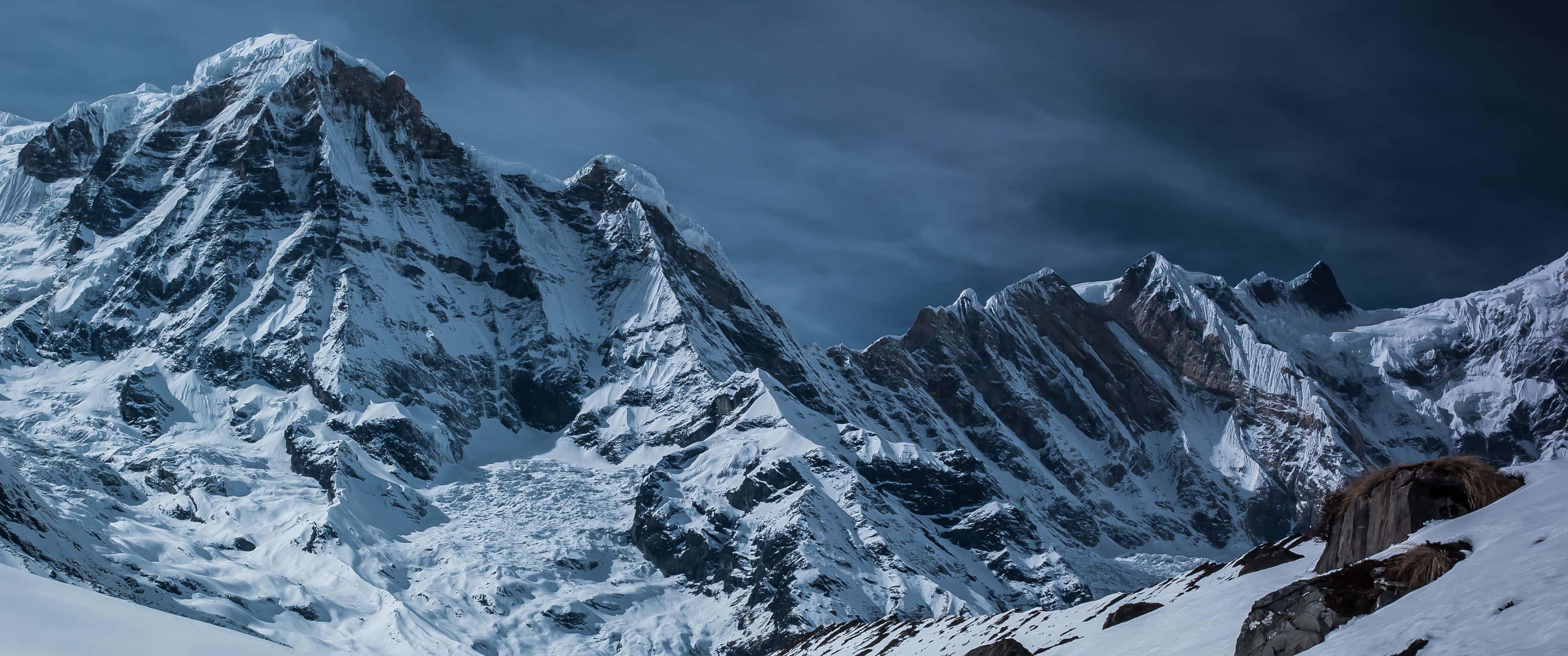令人驚嘆的 3440x1440 高清壁紙 壁紙 — 在陰暗的天空下，戲劇性的積雪山脈，帶有尖銳的山脊和冰冷的質感。