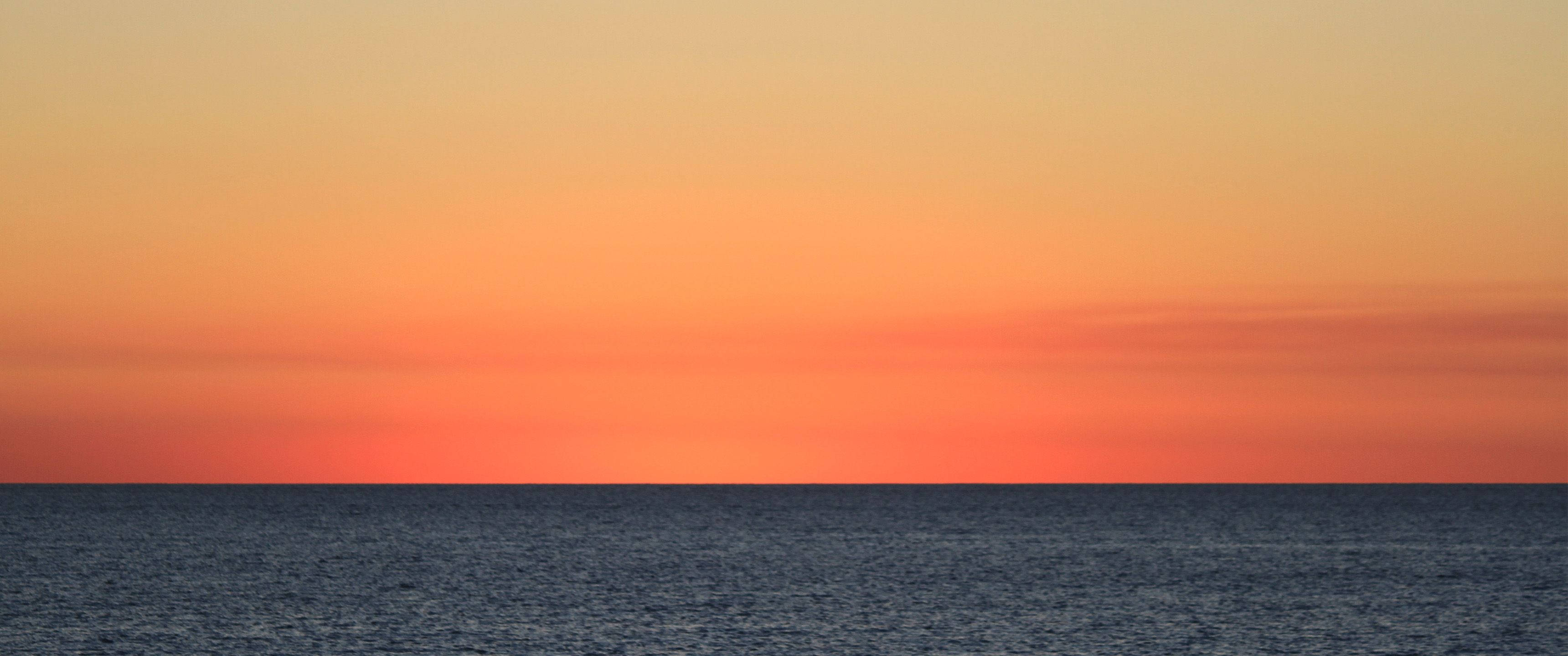 3440x1440 极简主義橙色海天 壁紙 — 平靜的日落，映照在平靜的海面上，呈現橙色和藍色的漸變色調。