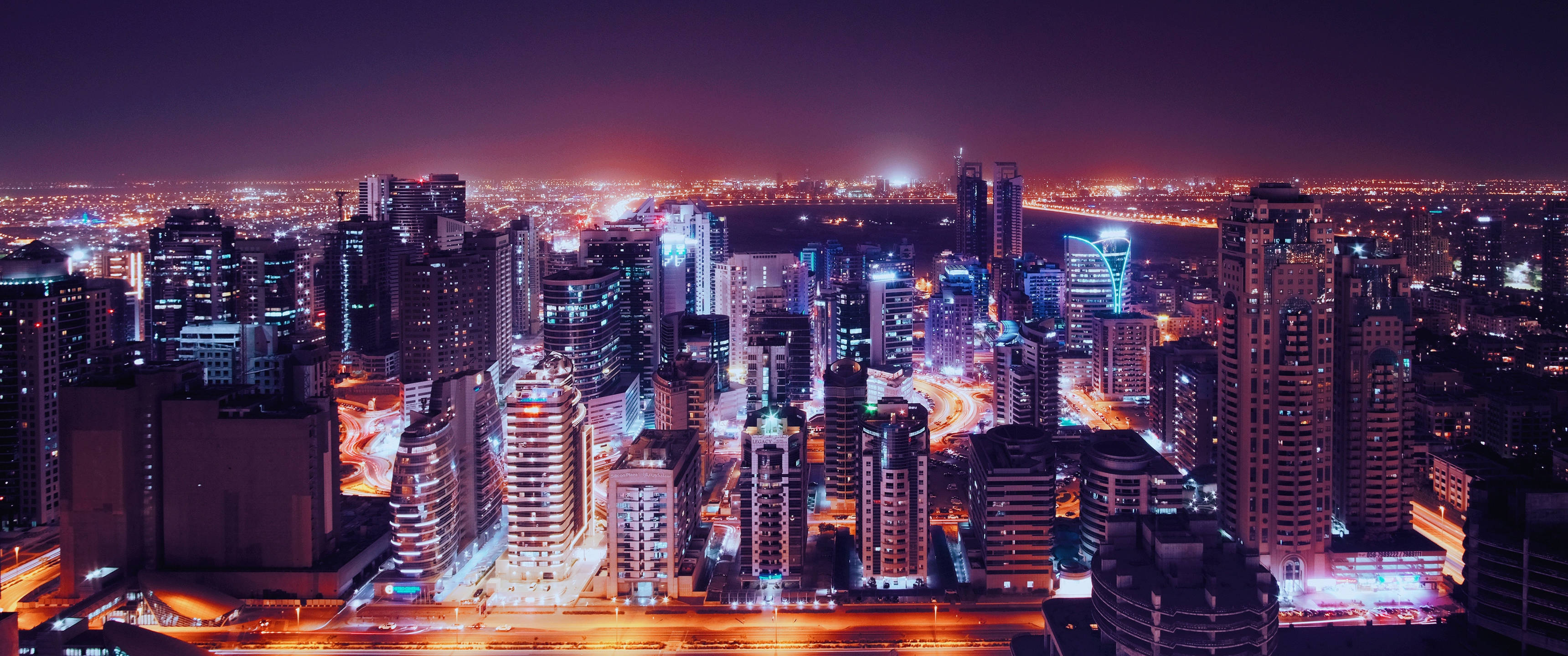 3440x1440 吉隆坡城市夜景 壁紙 — 深紫色天空下，閃爍的摩天大樓與燈火通明的街道交織而成的活力城市夜景全景。