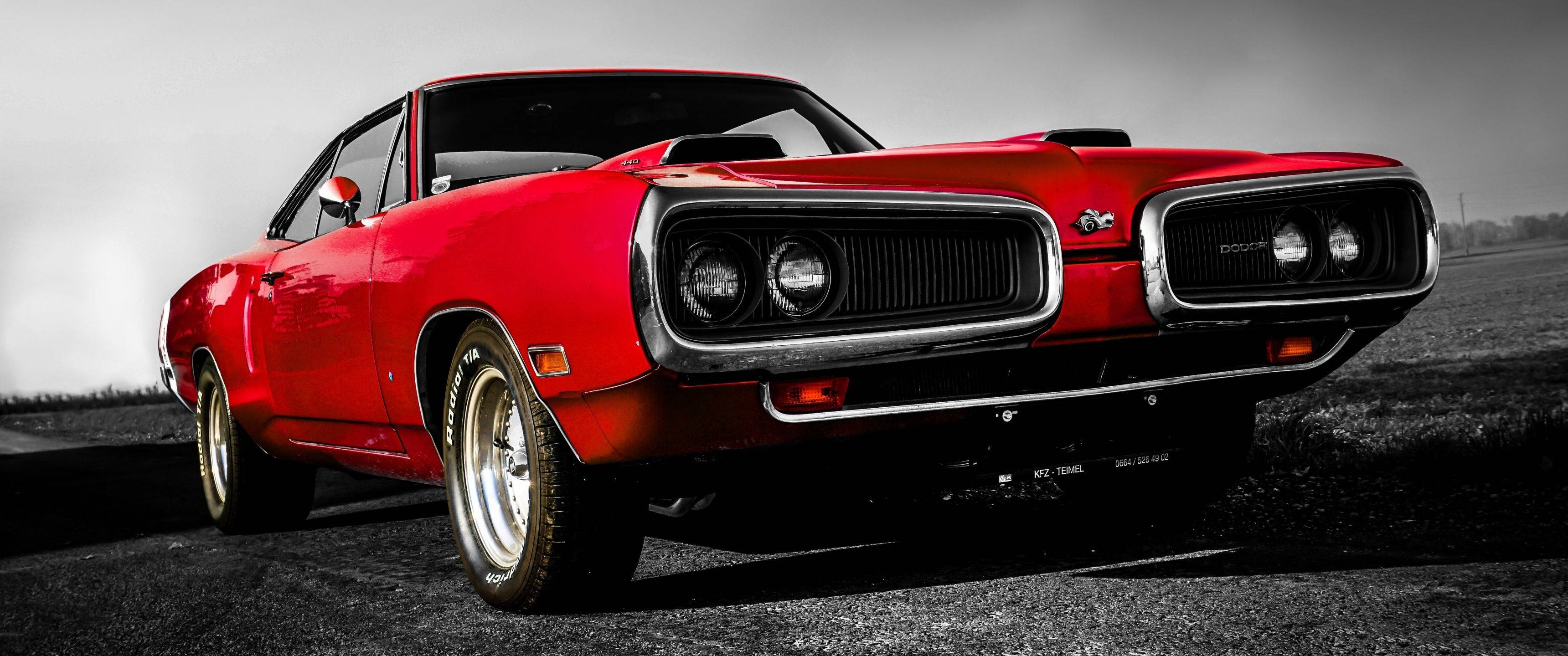3440x1440 道奇 Super Bee 跑車壁紙 壁紙 — 一輛充滿活力的紅色經典肌肉車，帶有鍍鉻細節，在陰沉天空下大膽地停在荒涼的道路上。