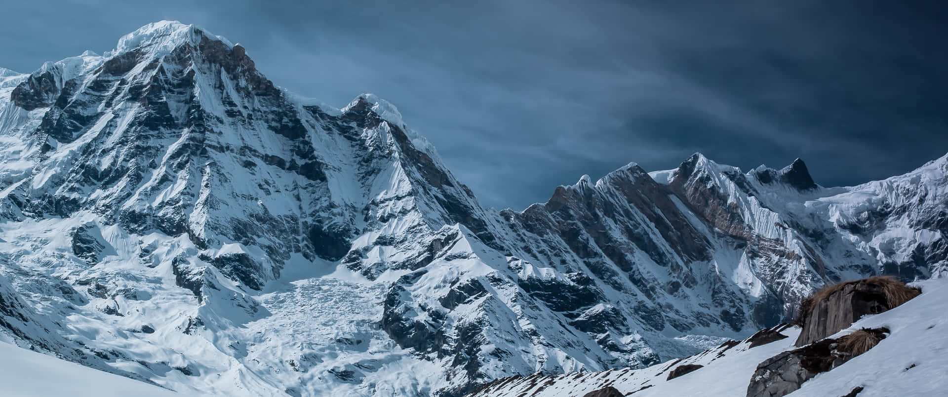 多雲的天空下，積雪的山峰上有岩石露頭。
