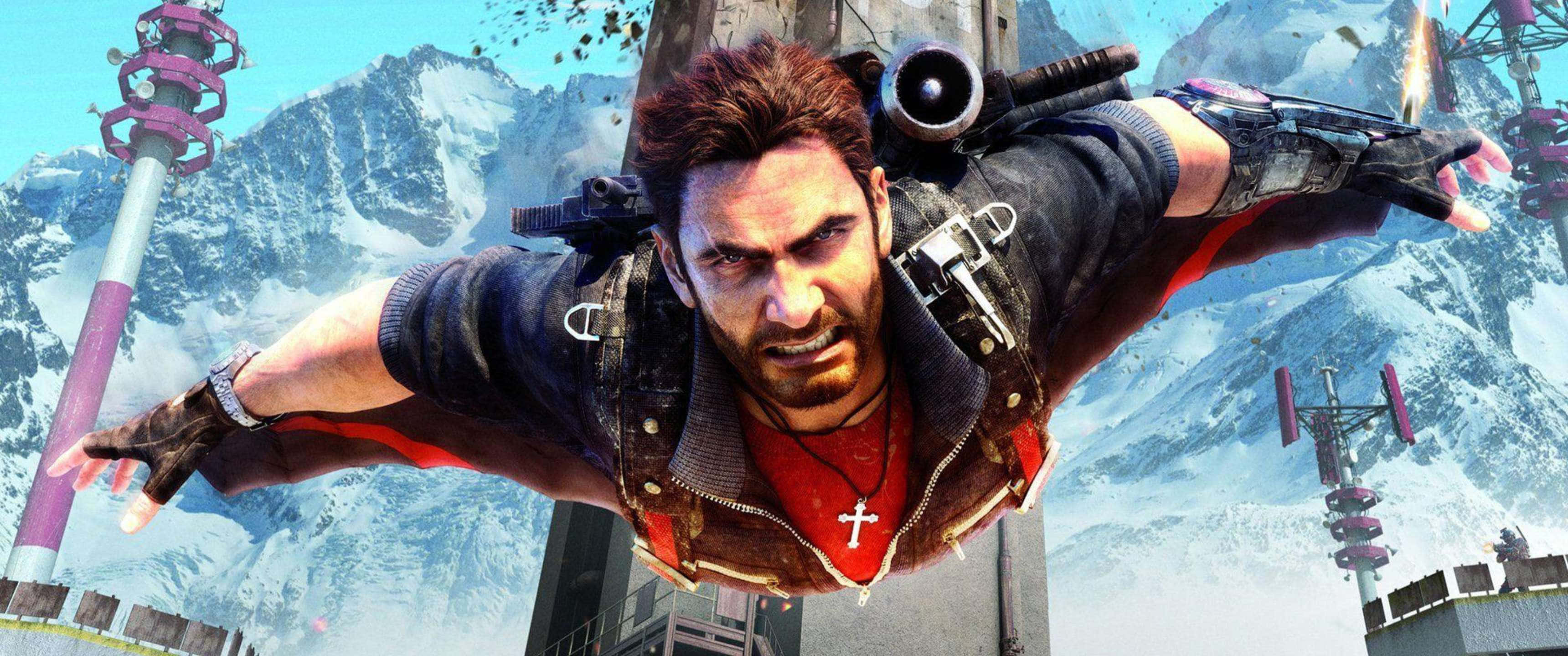 3440x1440p《Just Cause 4》混亂特工背景 壁紙 — 一個粗獷的男人戴著十字架項鍊，在白雪覆蓋的山脈和未來主義塔樓的背景下翱翔於空中。