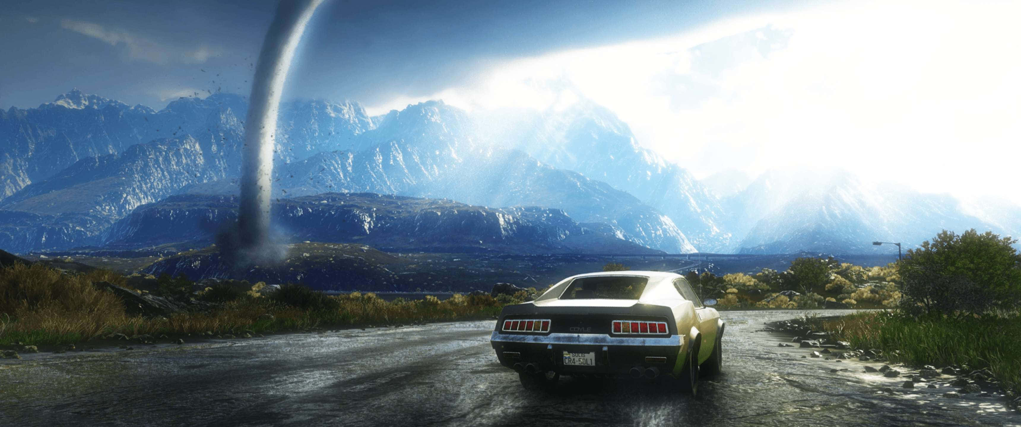 3440x1440p《Just Cause 4》古董車行駛背景 壁紙 — 一輛經典肌肉車在明亮的陽光下，朝著高聳的龍捲風行駛，背景是戲劇性的山脈。
