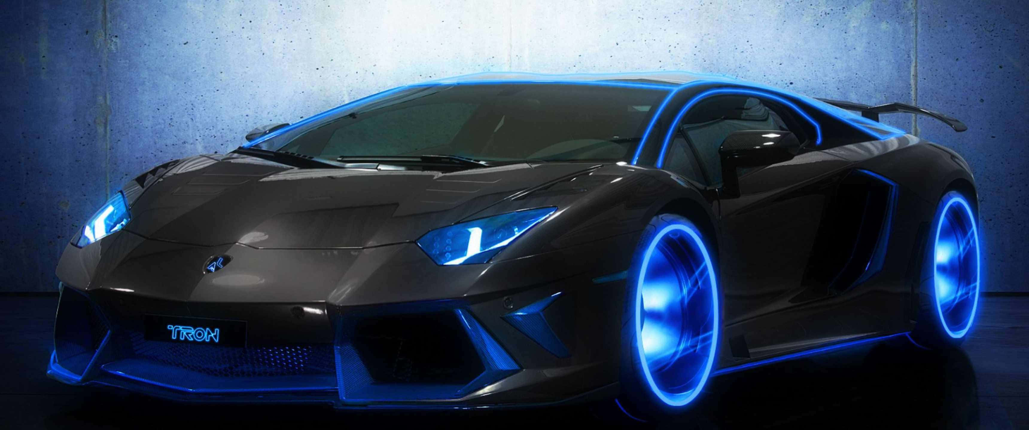 欣賞 3440x1440p 蘭博基尼的絕美風采 壁紙 — 一架時尚的黑色跑車，輪圈和車頭燈發出藍色霓虹燈光，靠著紋理混凝土牆。